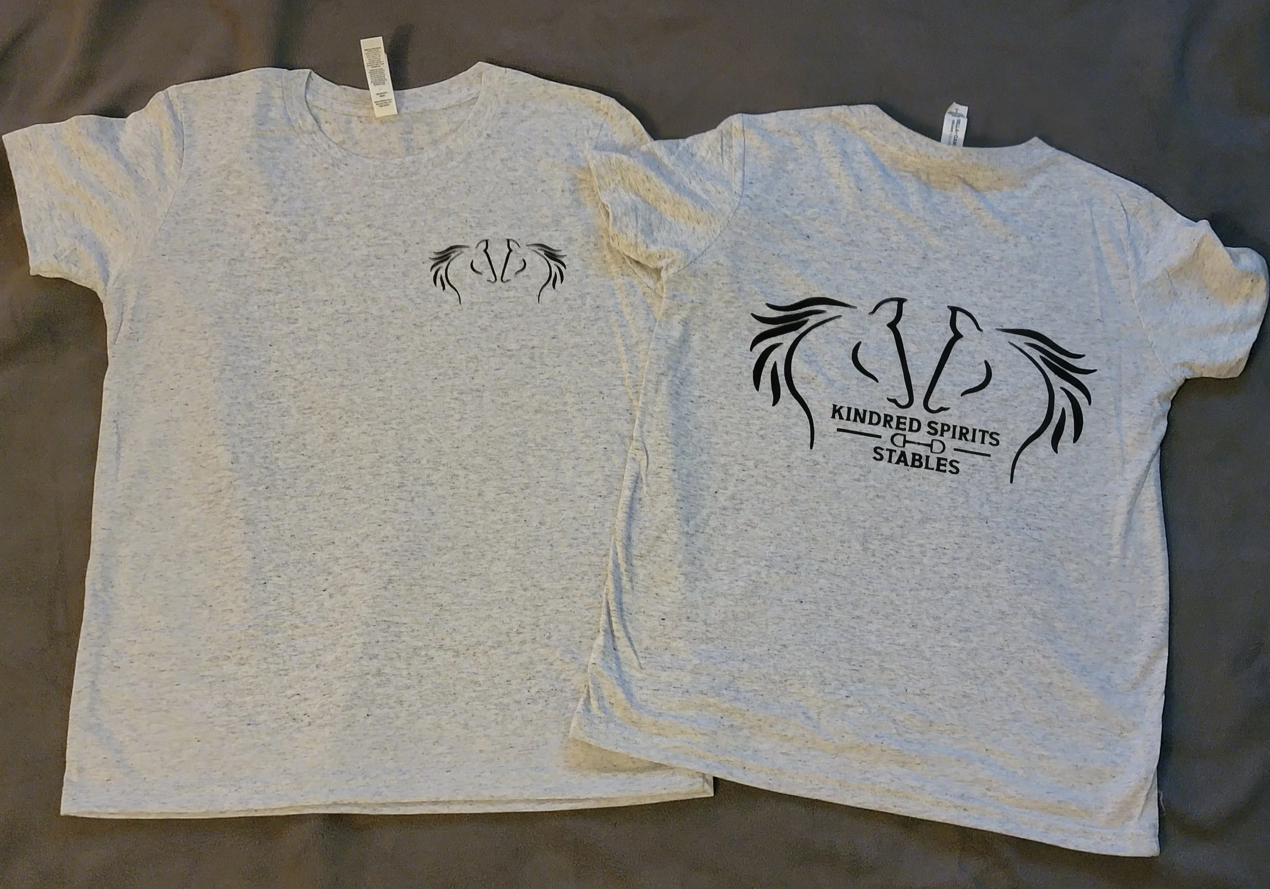 Gray T-shirts with horse head and mane designs, one with a small design on the front and a larger one on the back that reads "KINDRED SPIRITS STABLES."
