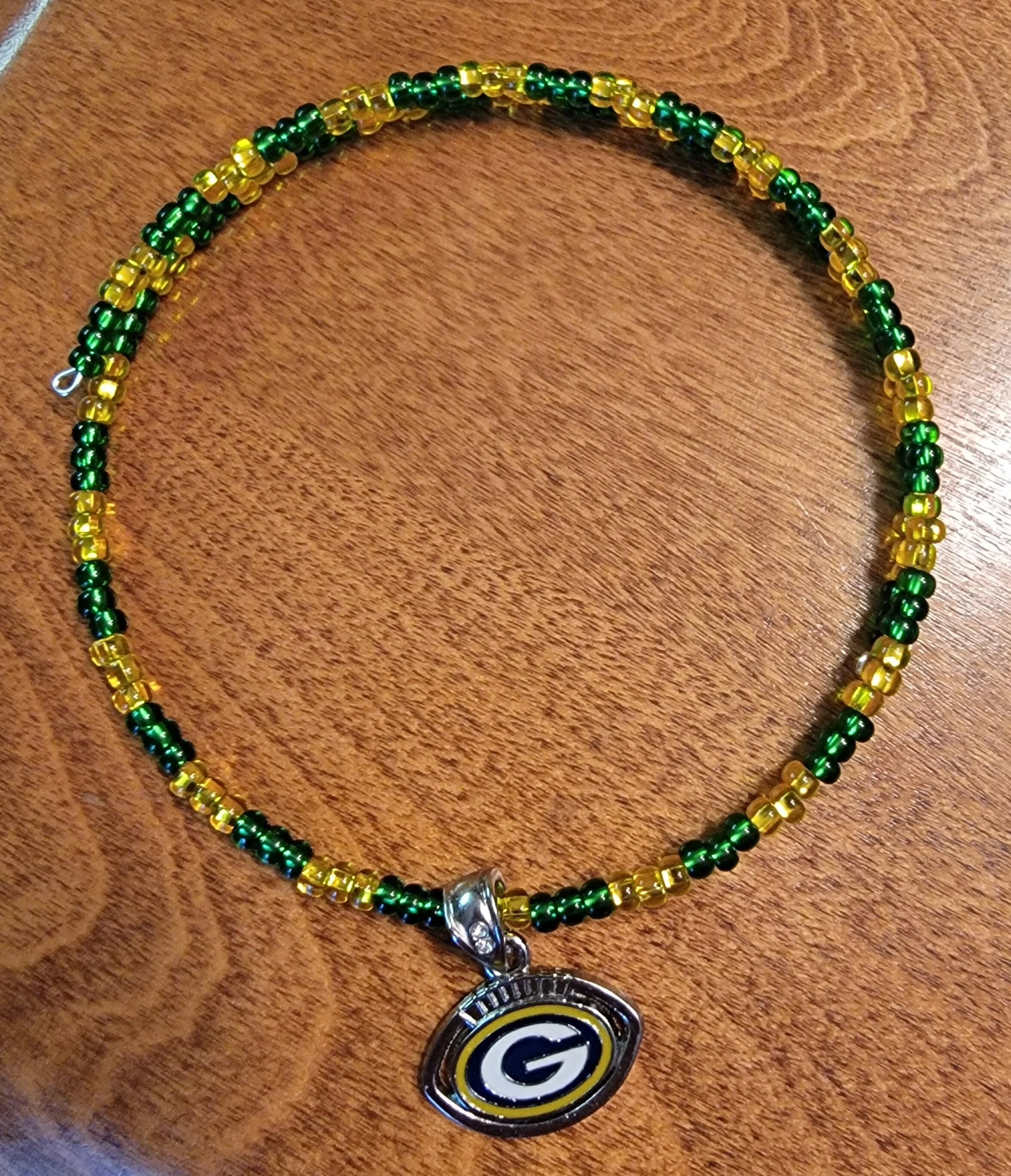 Beaded necklace with green and yellow beads and a Green Bay Packers logo pendant on a wooden surface.