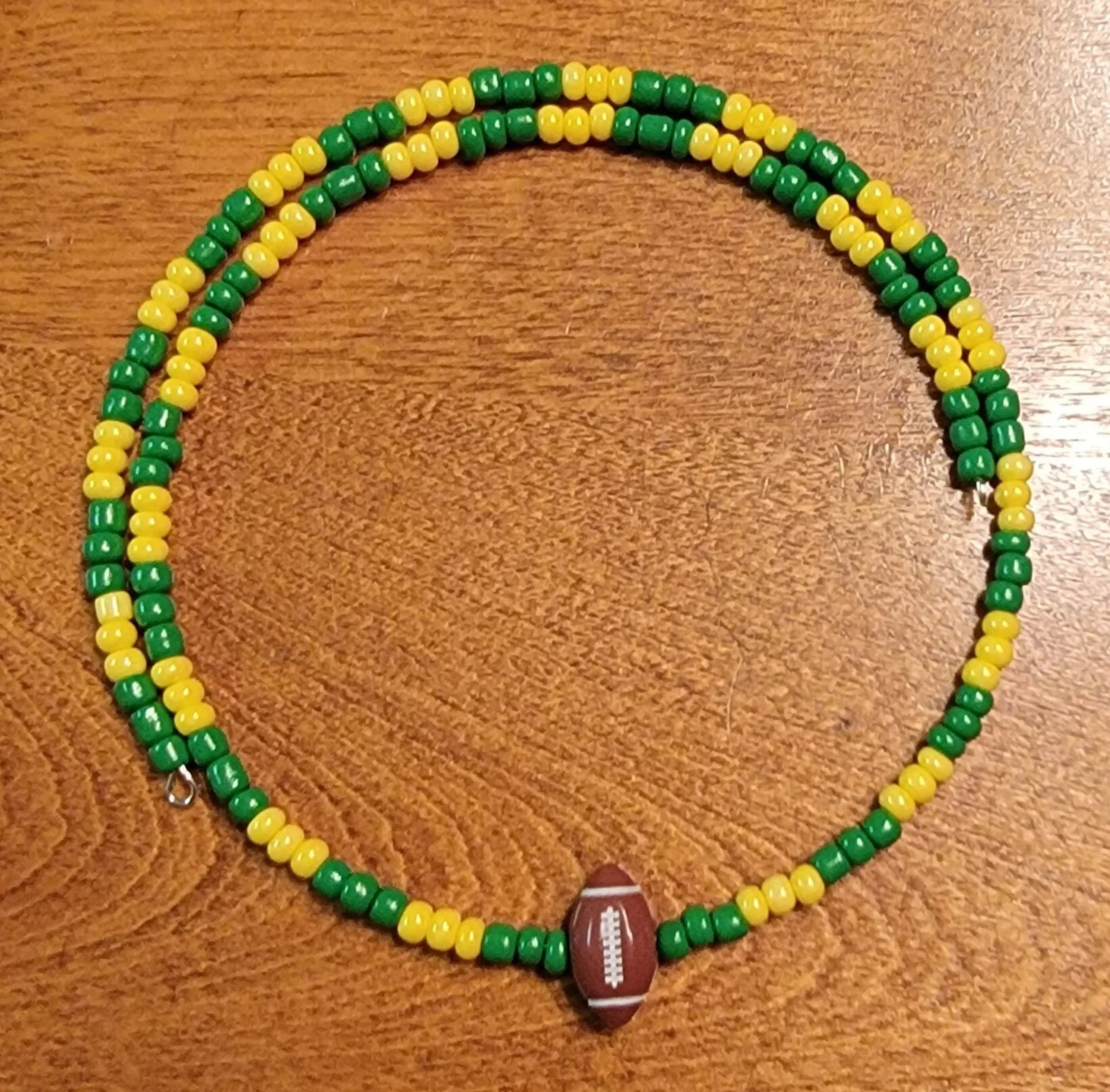Necklace with green and yellow beads and an oval football-shaped pendant.