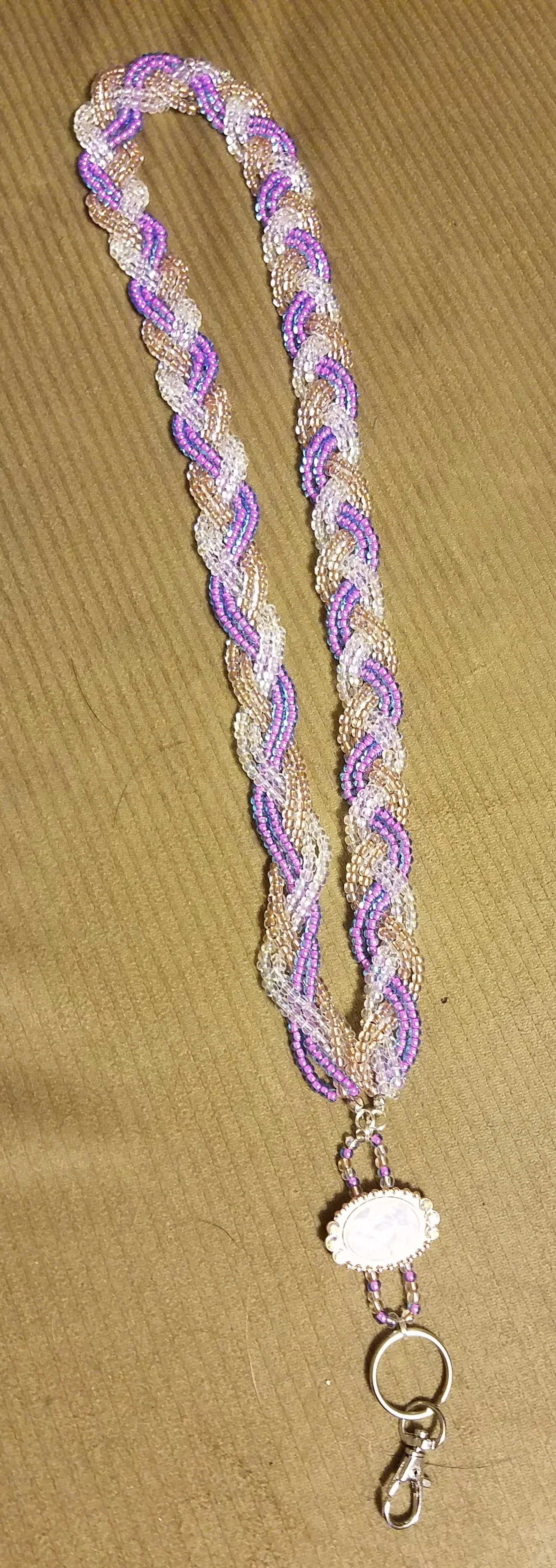 Beaded necklace with purple, pink, and pearl-colored beads on a brown fabric surface.
