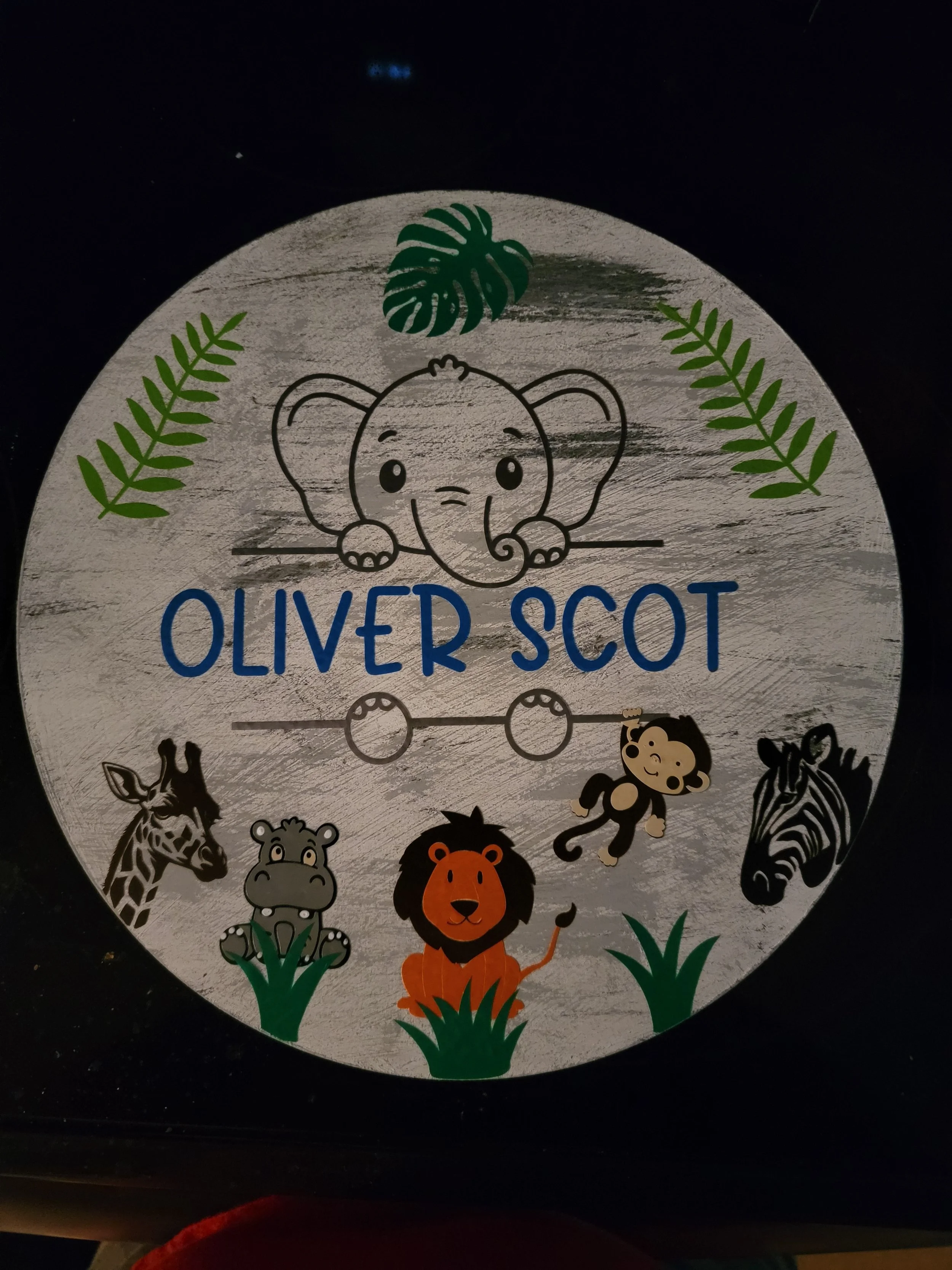 Decorative sticker featuring a cartoon elephant with the text "Oliver Scot" and illustrations of a zebra, cheetah, hippopotamus, lion, and monkey surrounded by tropical leaves.