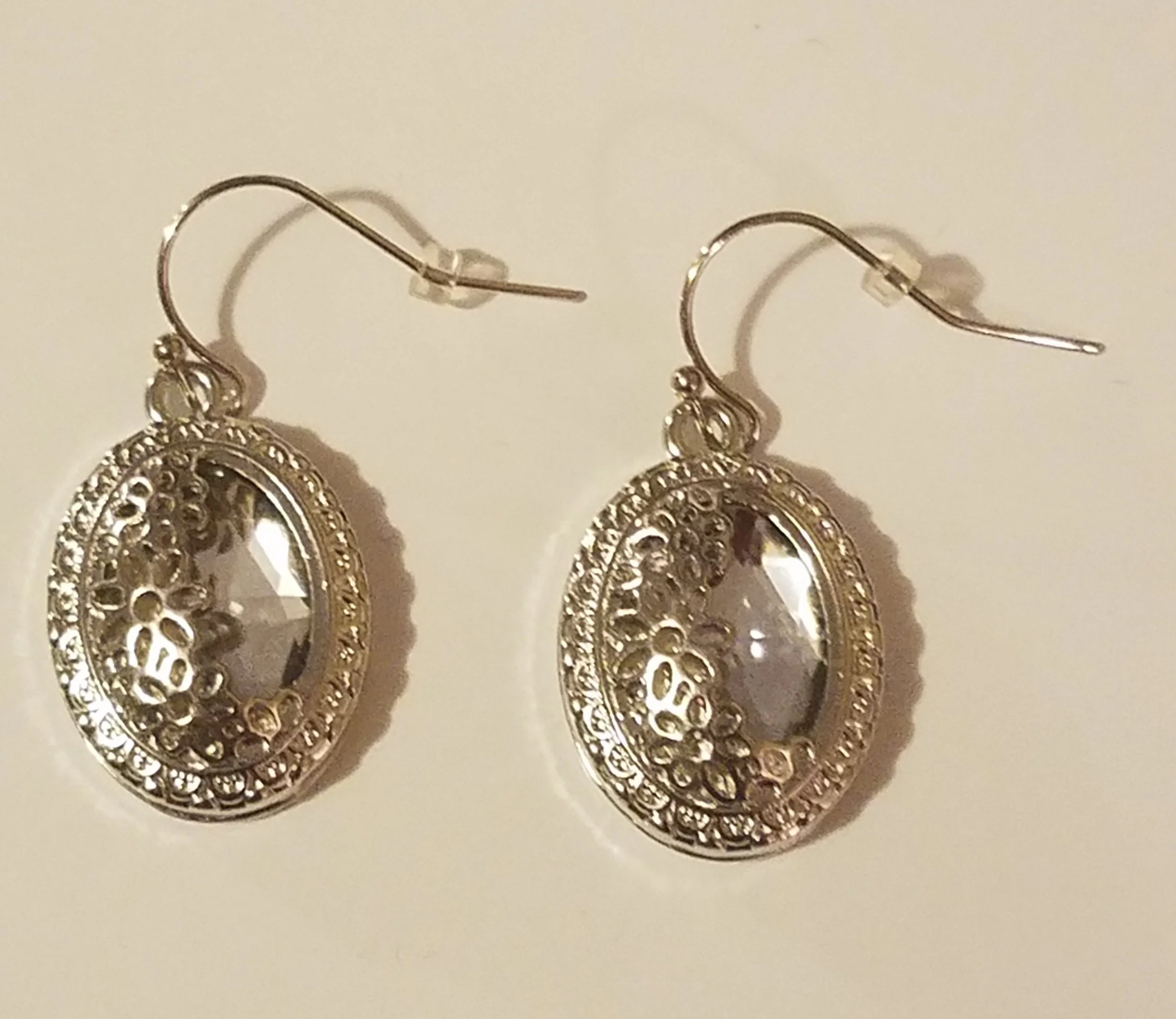 Silver dangling earrings with oval-shaped clear gemstones and ornate decorative details.