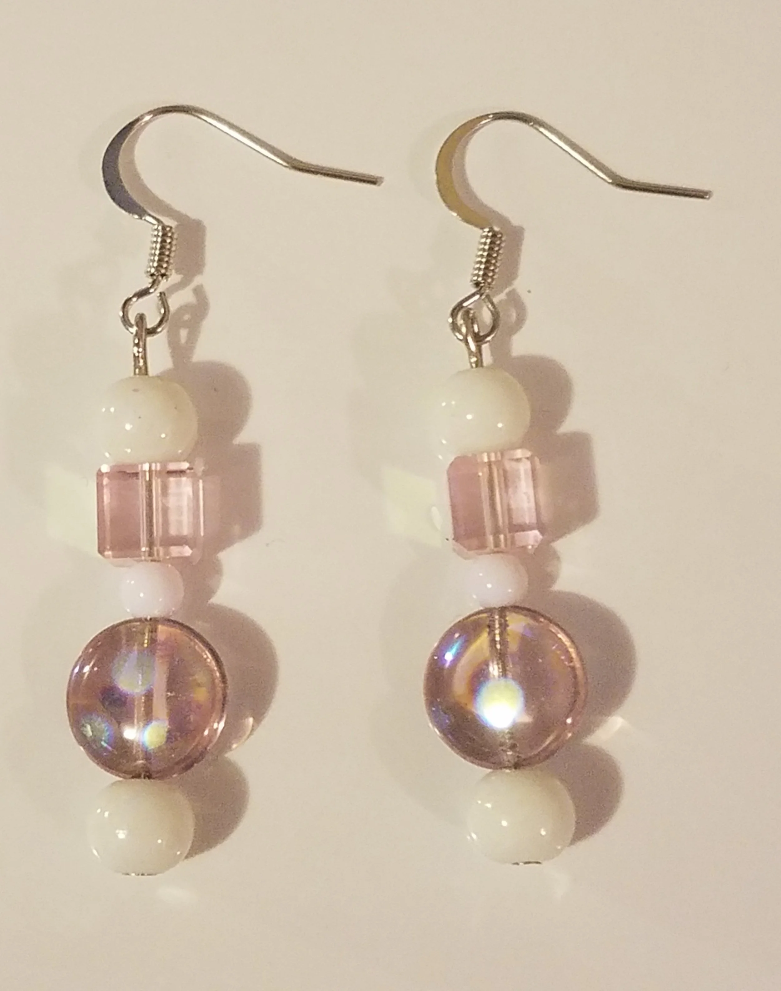 A pair of dangling earrings with pink, white, and iridescent beads.