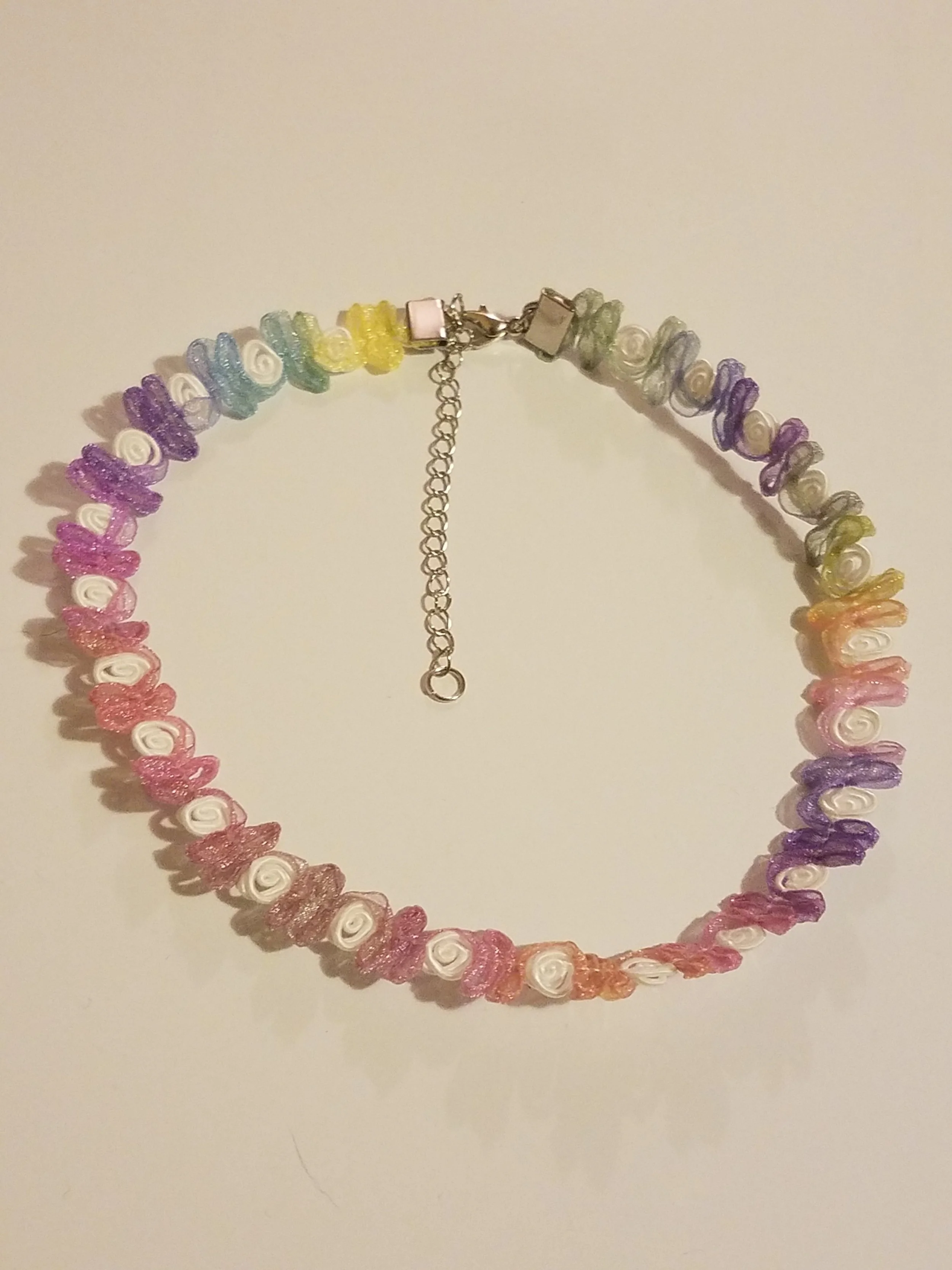 Colorful beaded necklace with a variety of pastel-colored flower-shaped beads arranged in a rainbow order, with a silver clasp and chain adjustment.