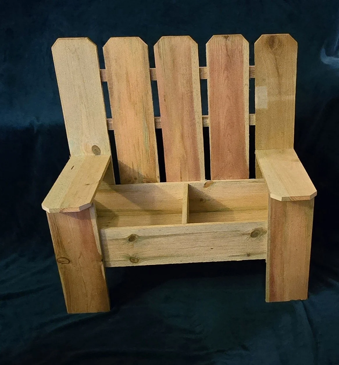 Wooden Adirondack-style chair with a small divided storage compartment in the seat, placed on a dark surface.