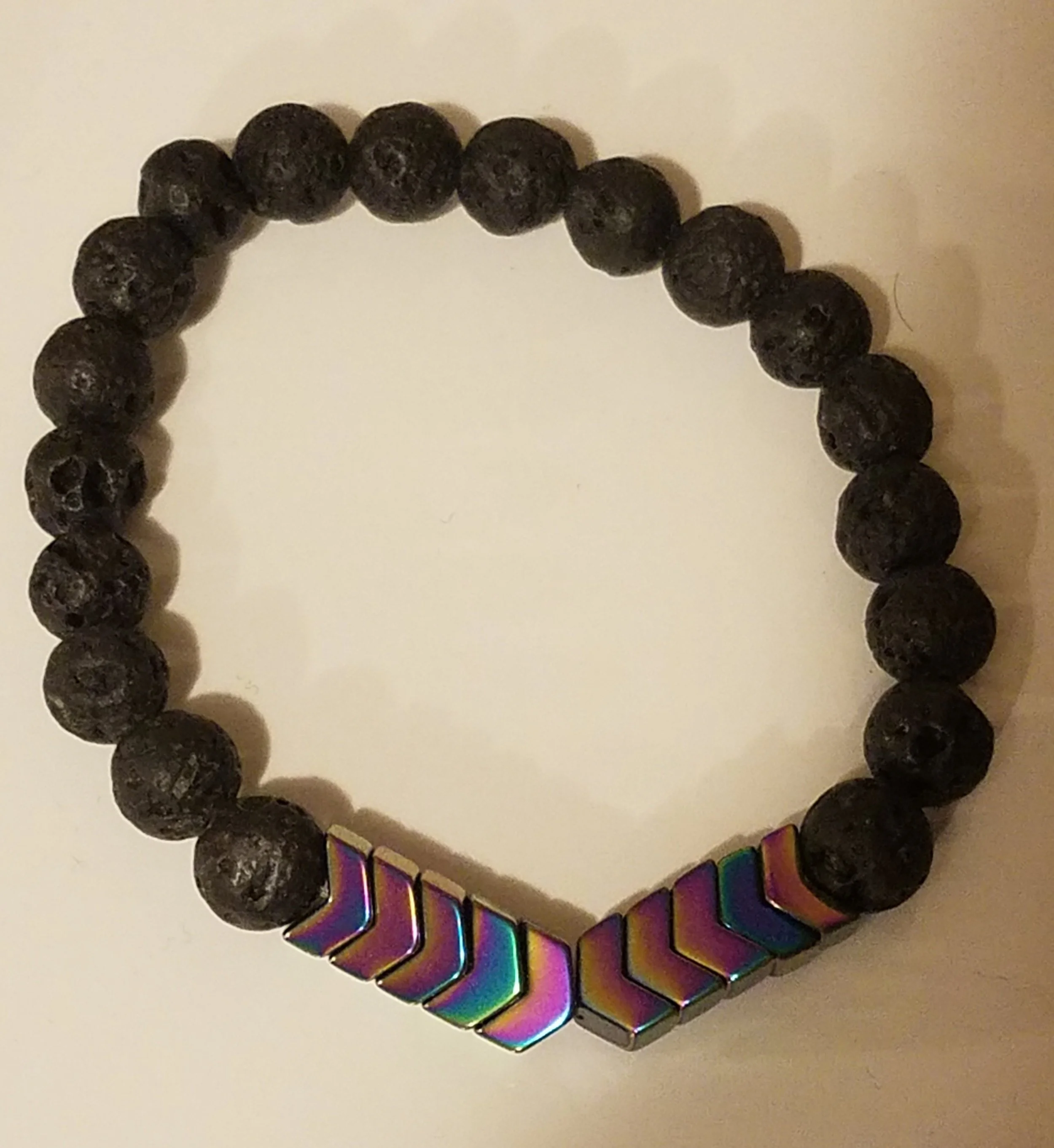 Black beaded bracelet with metallic, rainbow-colored rectangular beads at one end, arranged in a curve on a white surface.