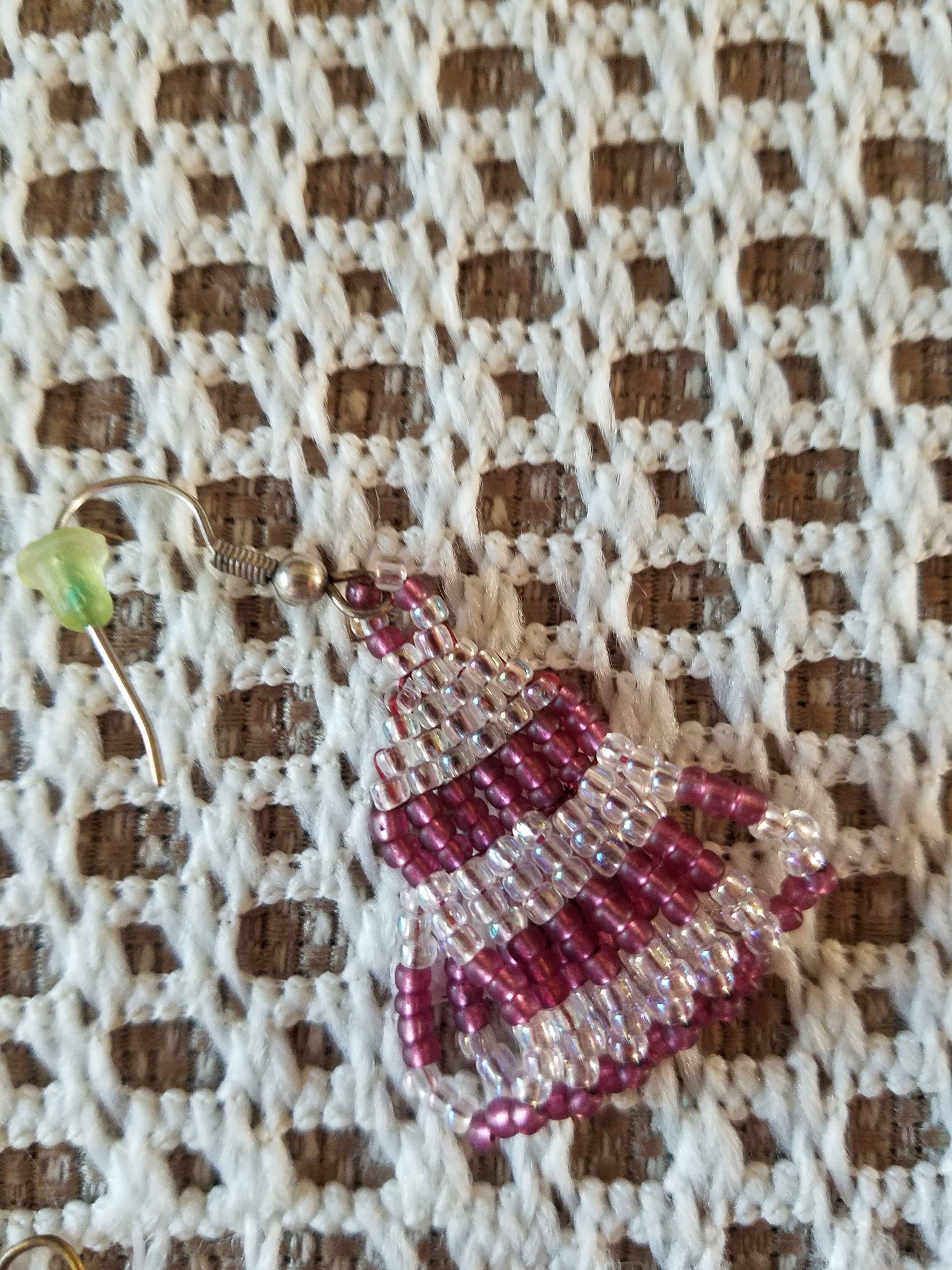 A beaded fish-shaped ornament made of pink and clear beads, placed on a woven fabric background.
