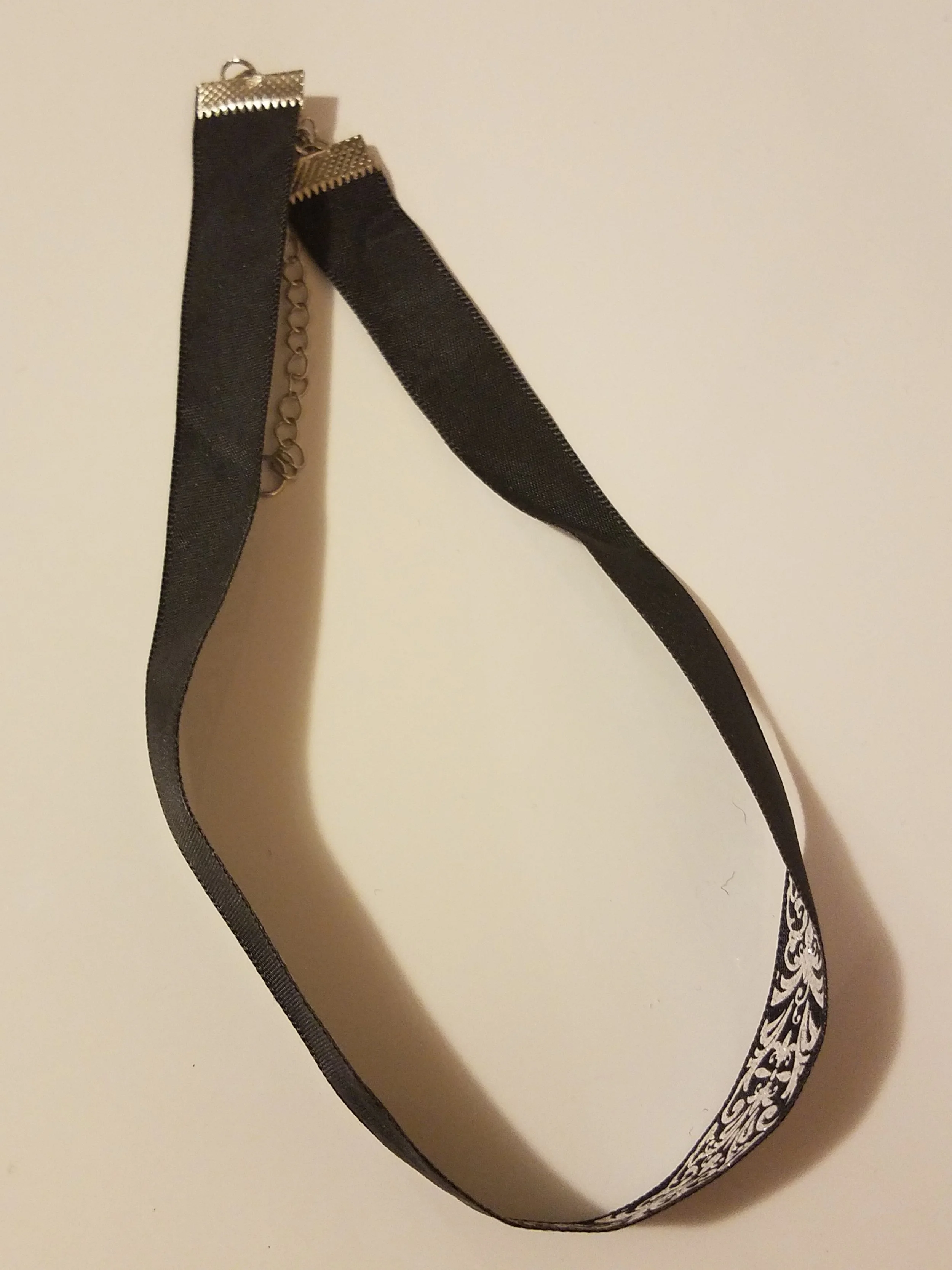A black choker necklace with a decorative white and black patterned end and metal clasps.