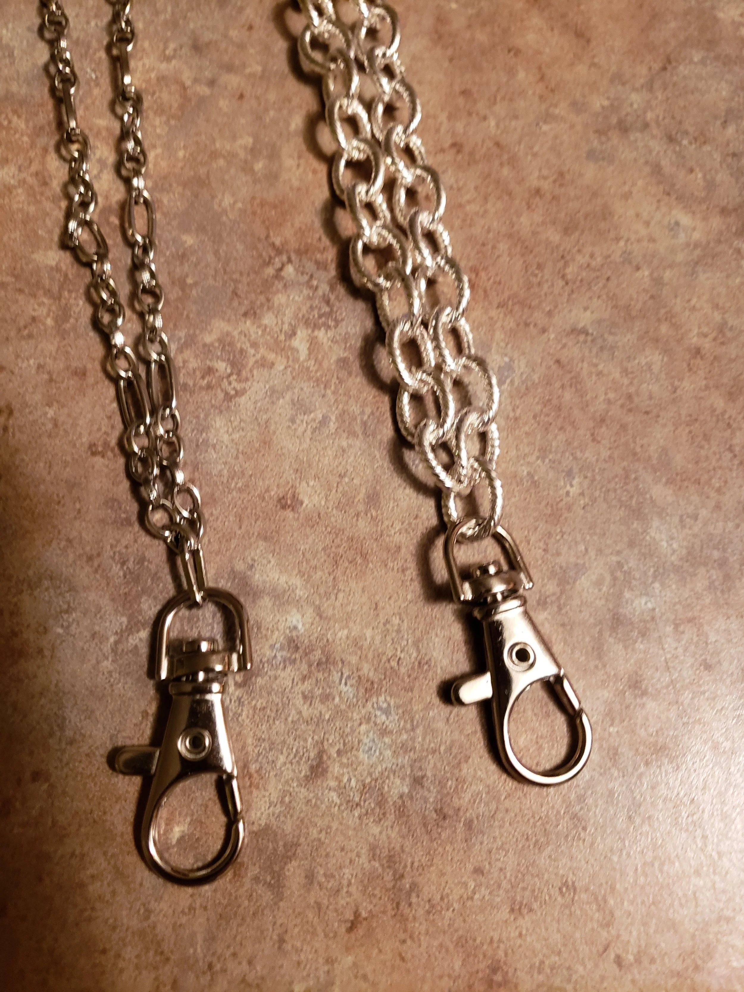 Two silver chains with lobster clasp clasps lying on a textured surface.