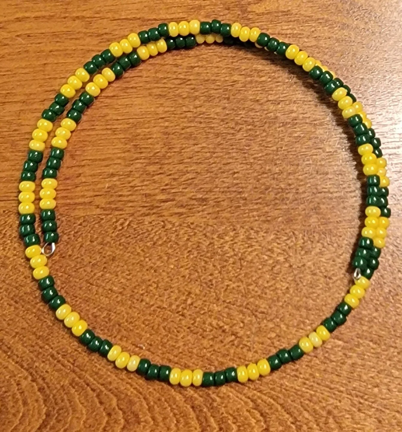 A beaded necklace with alternating yellow and green beads on a wooden surface.