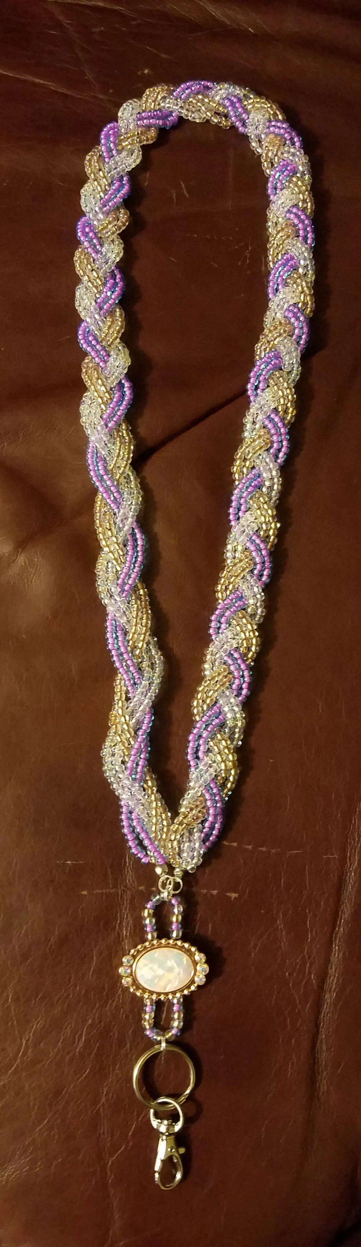 A beaded lanyard with pink, purple, gold, and clear beads, featuring a large oval-shaped mother of pearl pendant and a metal clasp.