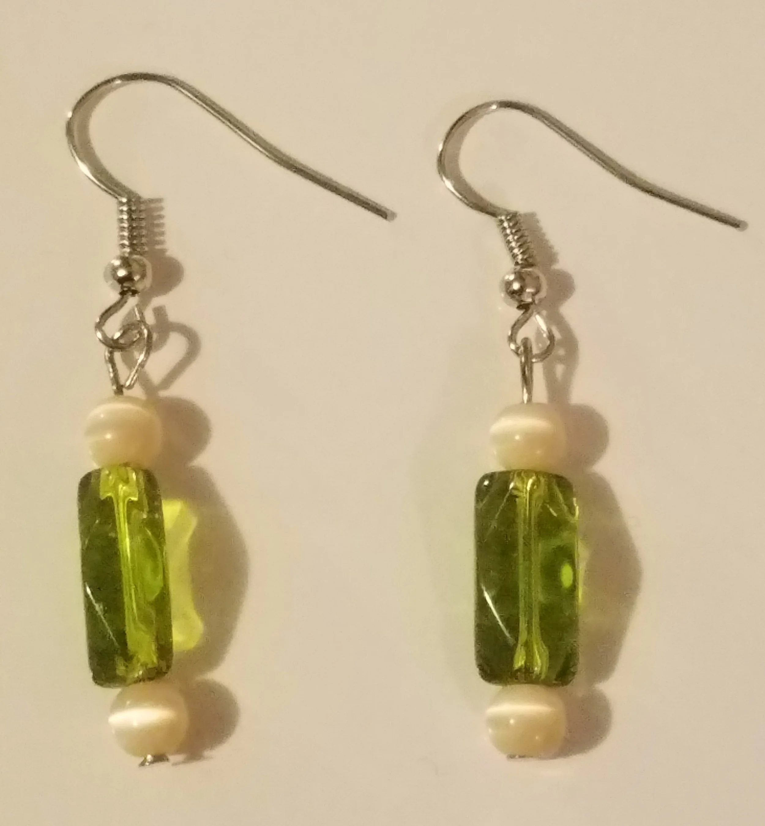 Pair of earrings with green rectangular beads, white round beads, and metal hooks.