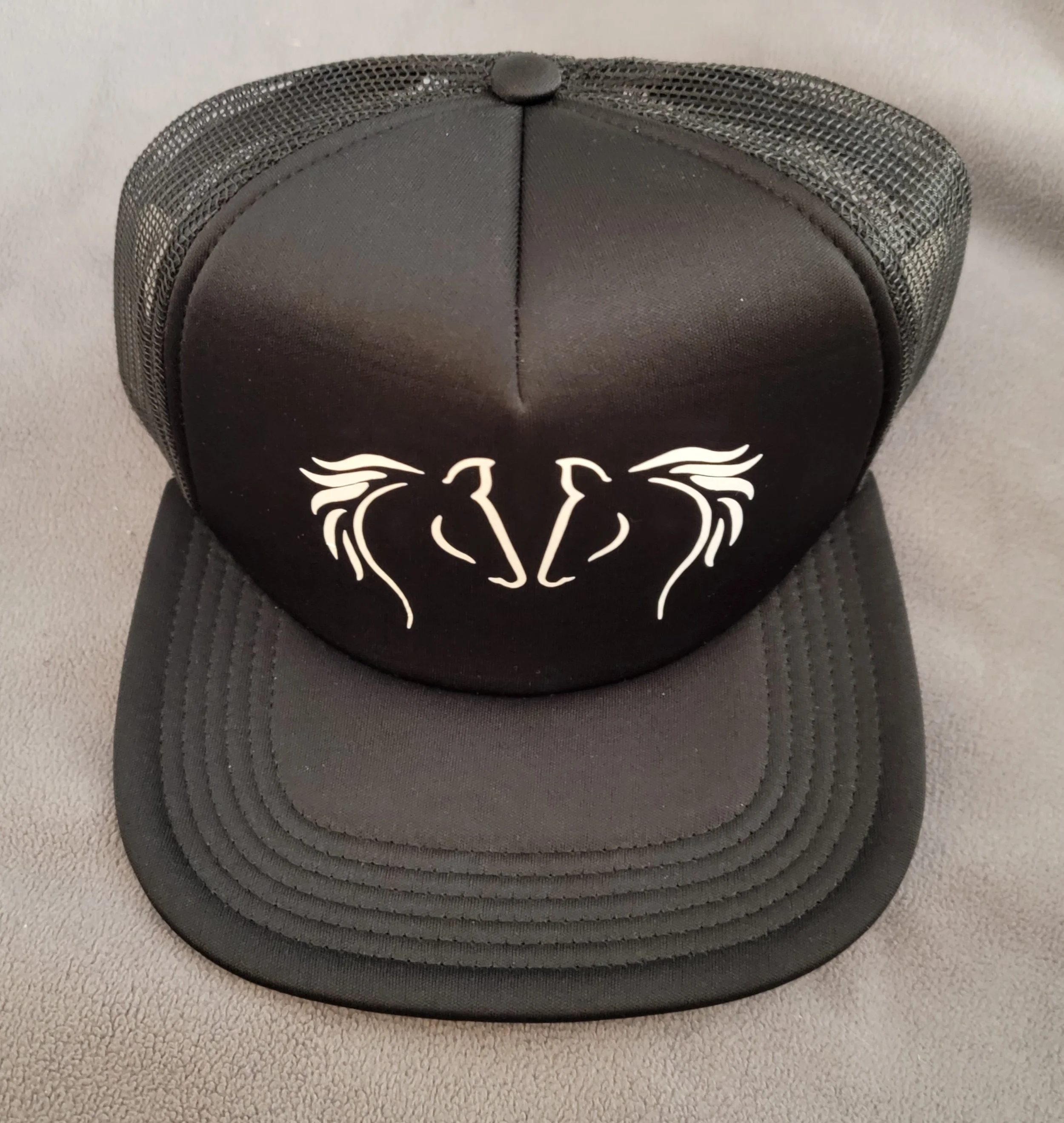 Black trucker-style baseball cap with white tribal horse head design on front panel, mesh back, and curved brim.