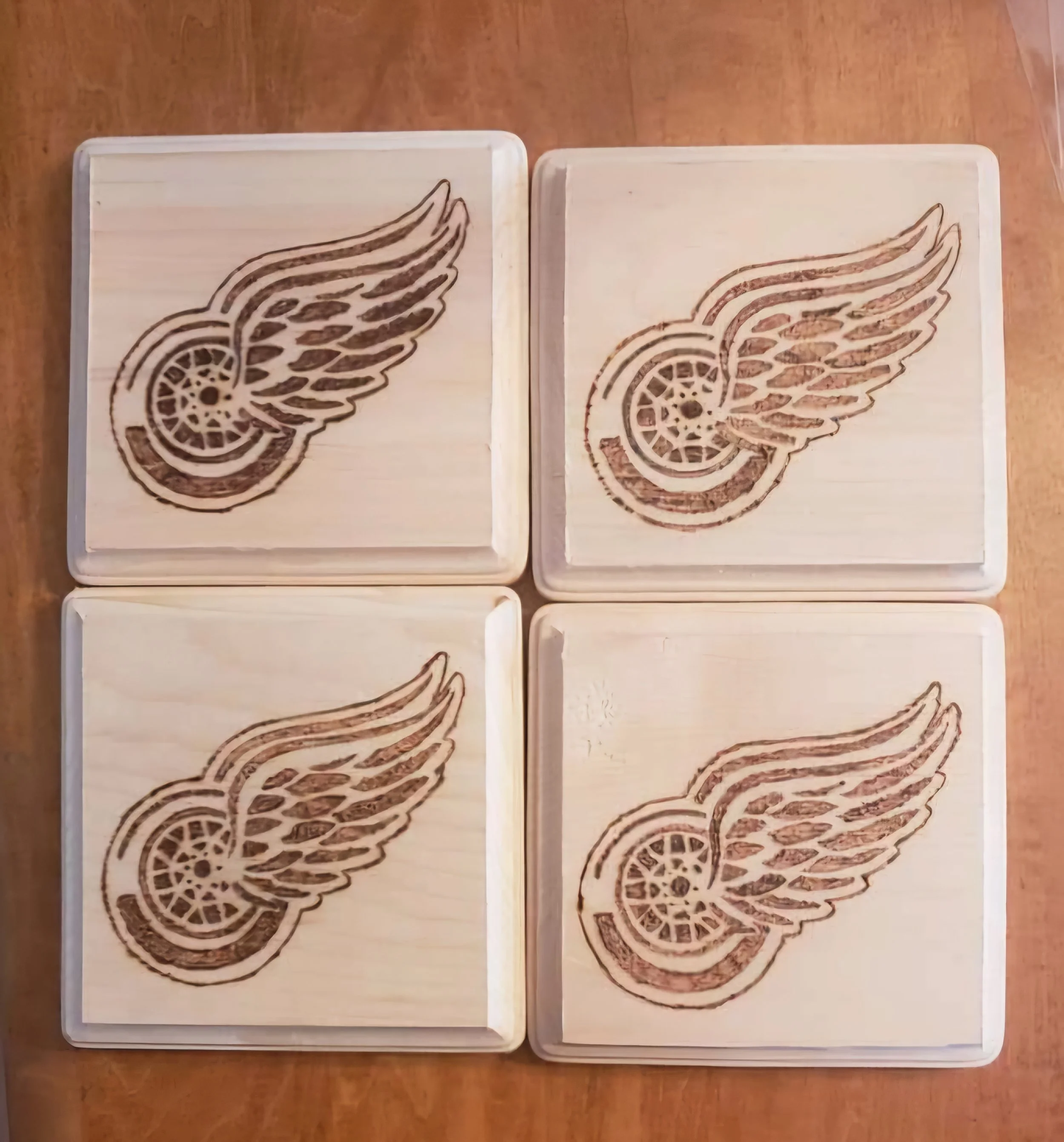 Four wooden blocks with the Detroit Red Wings logo burned into the surface, arranged in a 2x2 grid on a wooden table.