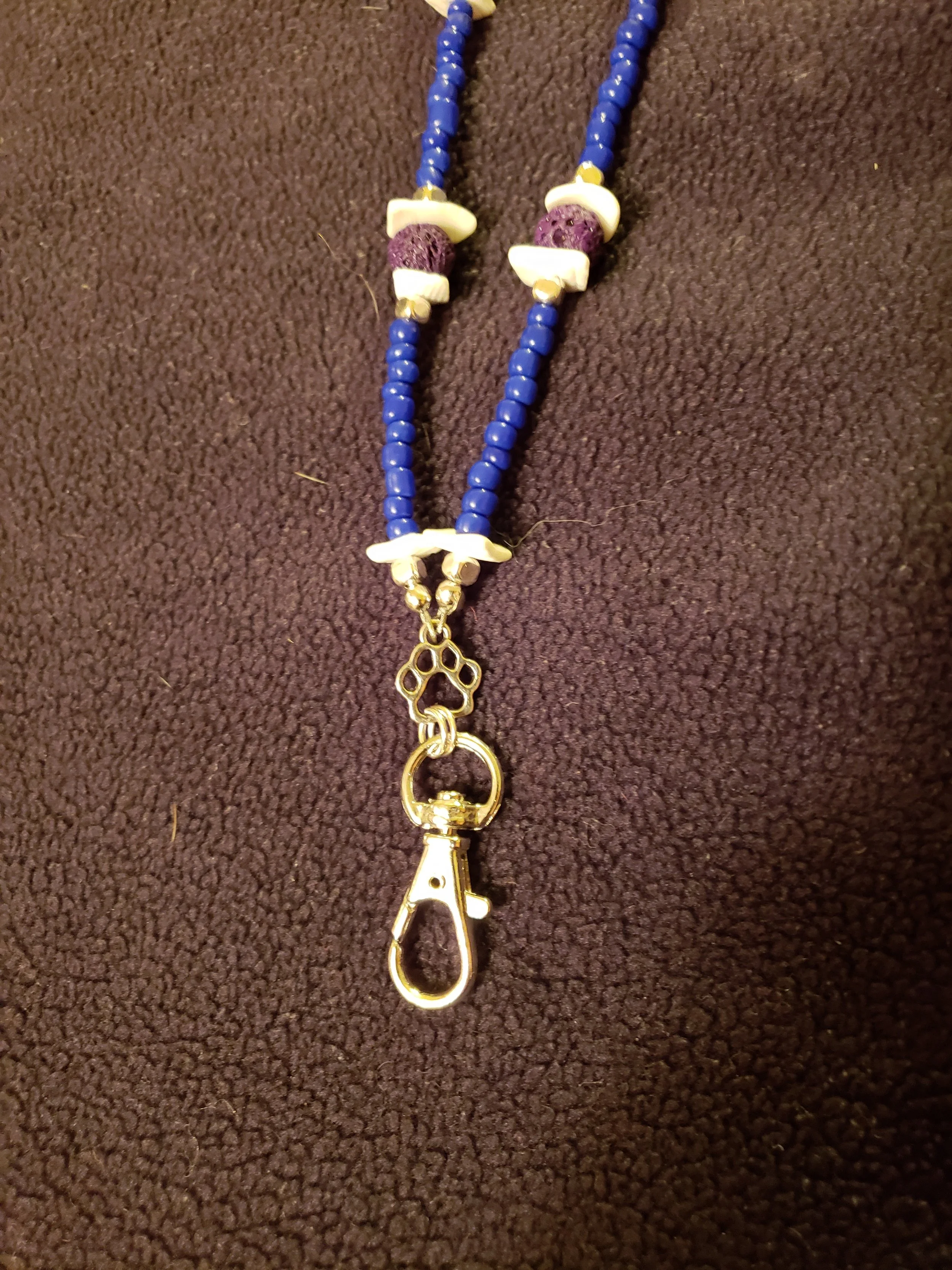 Colorful bead necklace with a silver clasp and a pendant in the shape of a paw print on a dark brown fabric background.