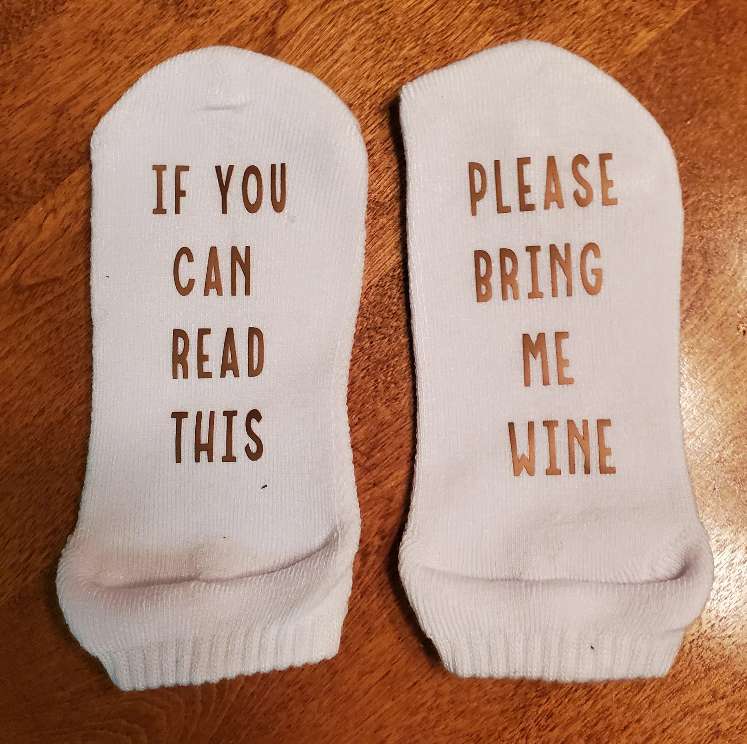 Pair of white socks, one says 'If you can read this', the other says 'Please bring me wine' in brown text.