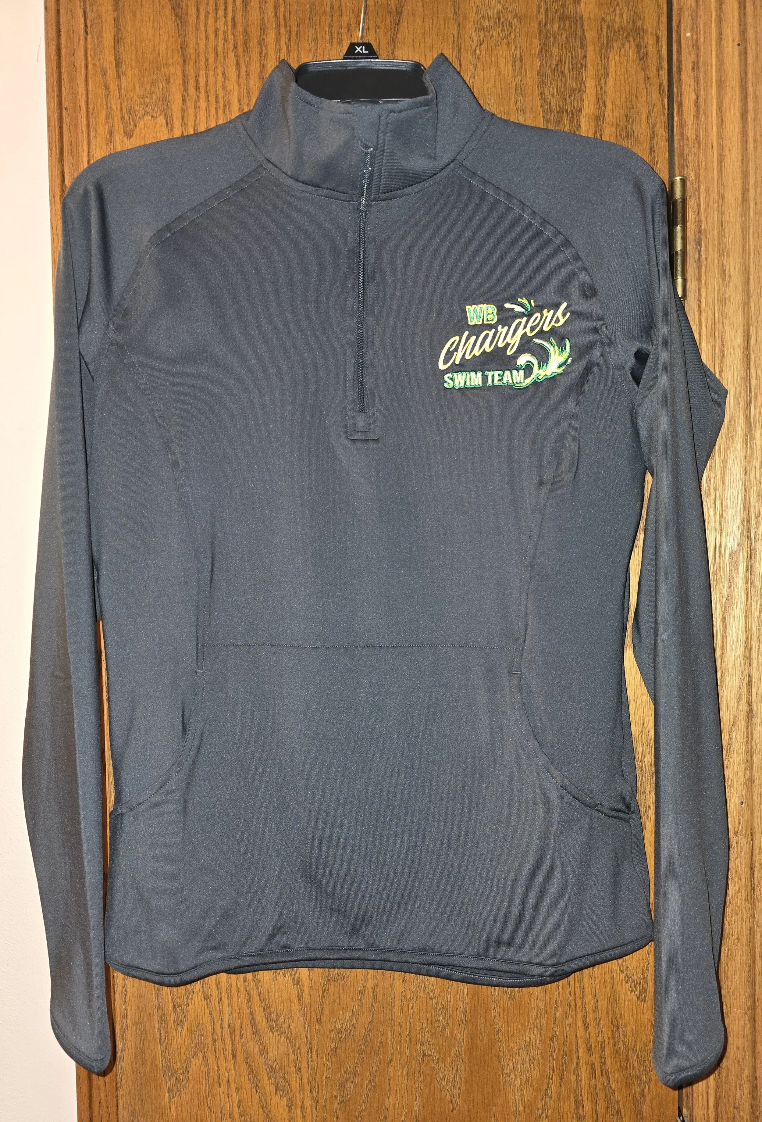 Gray quarter-zip athletic pullover with WB Chargers Swim Team logo embroidered on the left chest hanging on a black hanger on a wood door.