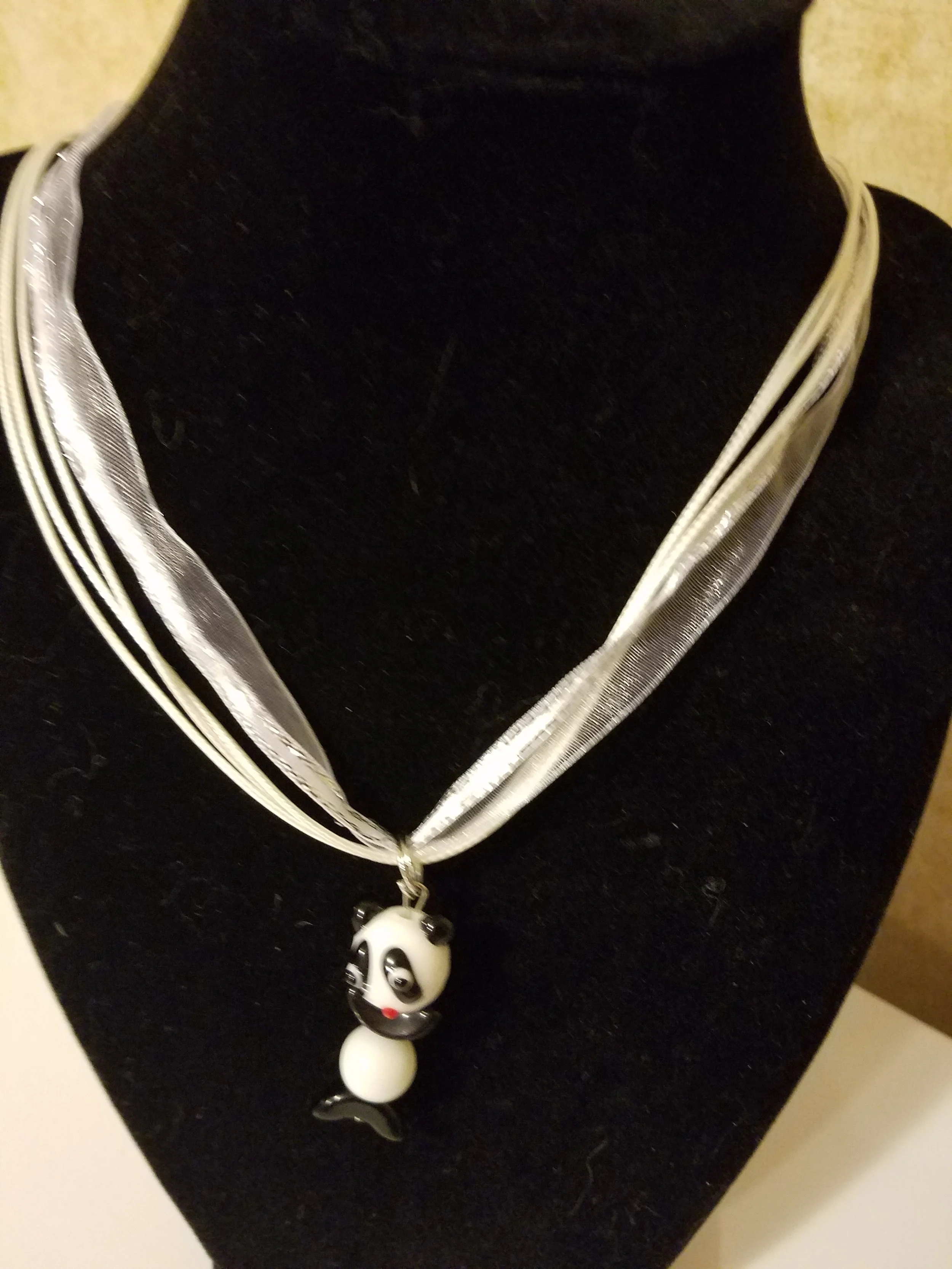 A necklace with a panda bear pendant displayed on a black bust. The necklace appears to be made of multiple silver or gray strands.