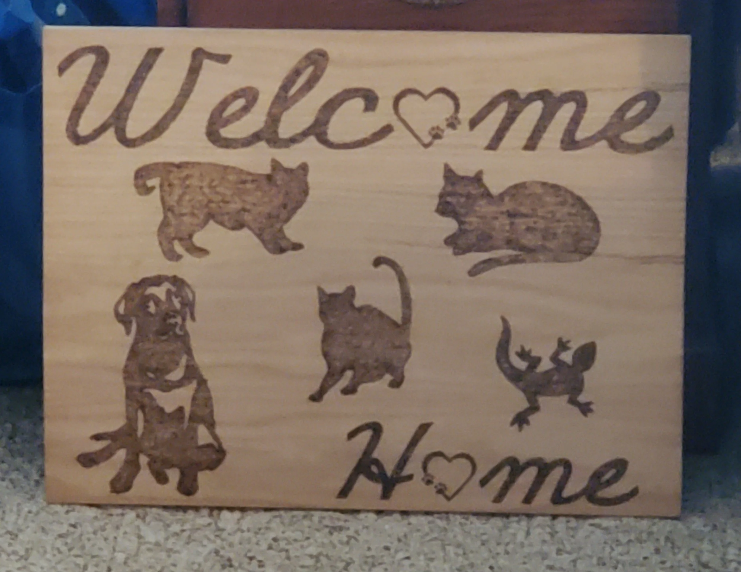 Wooden welcome sign with silhouettes of various animals and the words "Welcome" and "Home" decorated with heart shapes