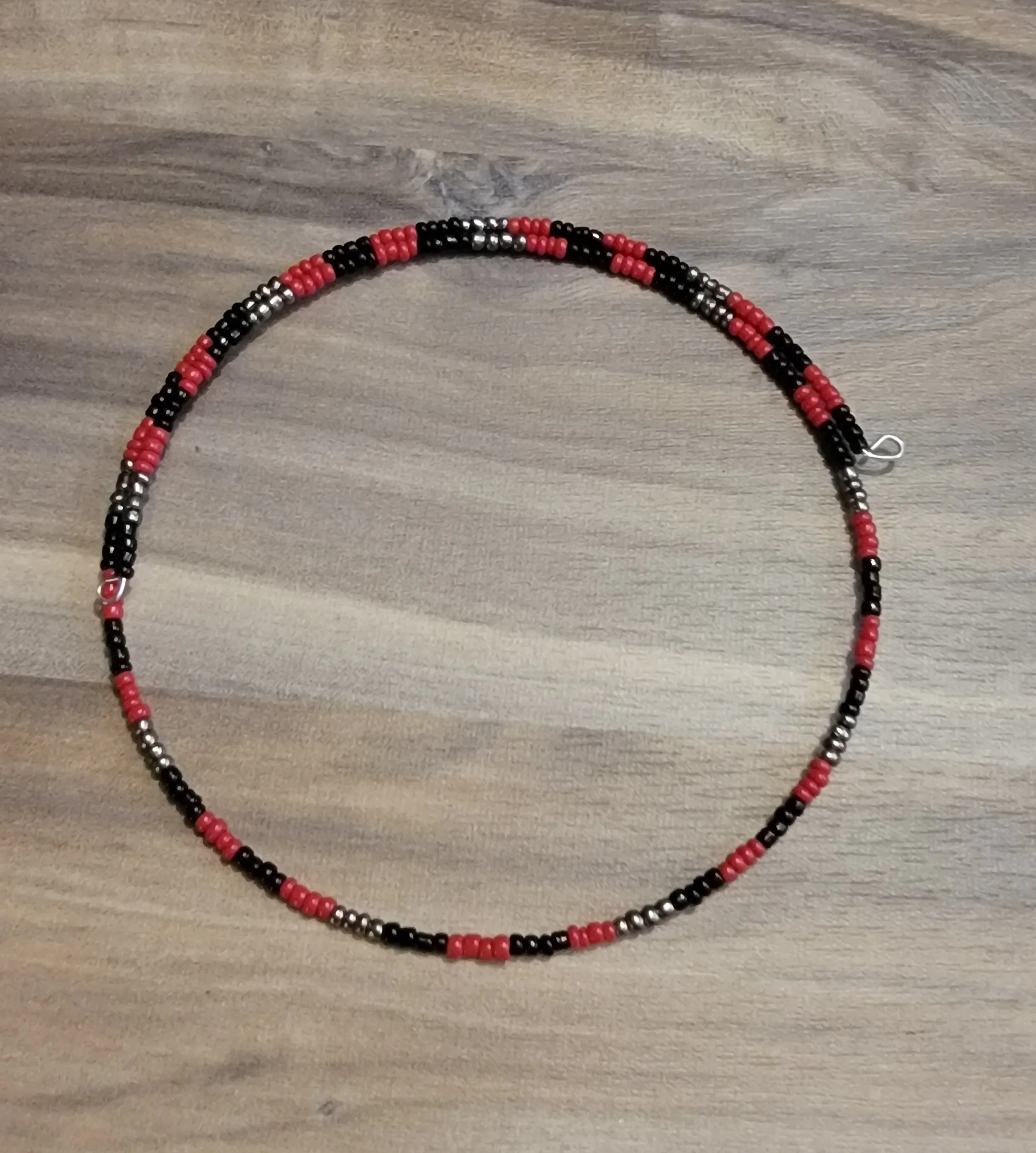 Beaded necklace with red, black, silver, and pink beads on a wooden surface.