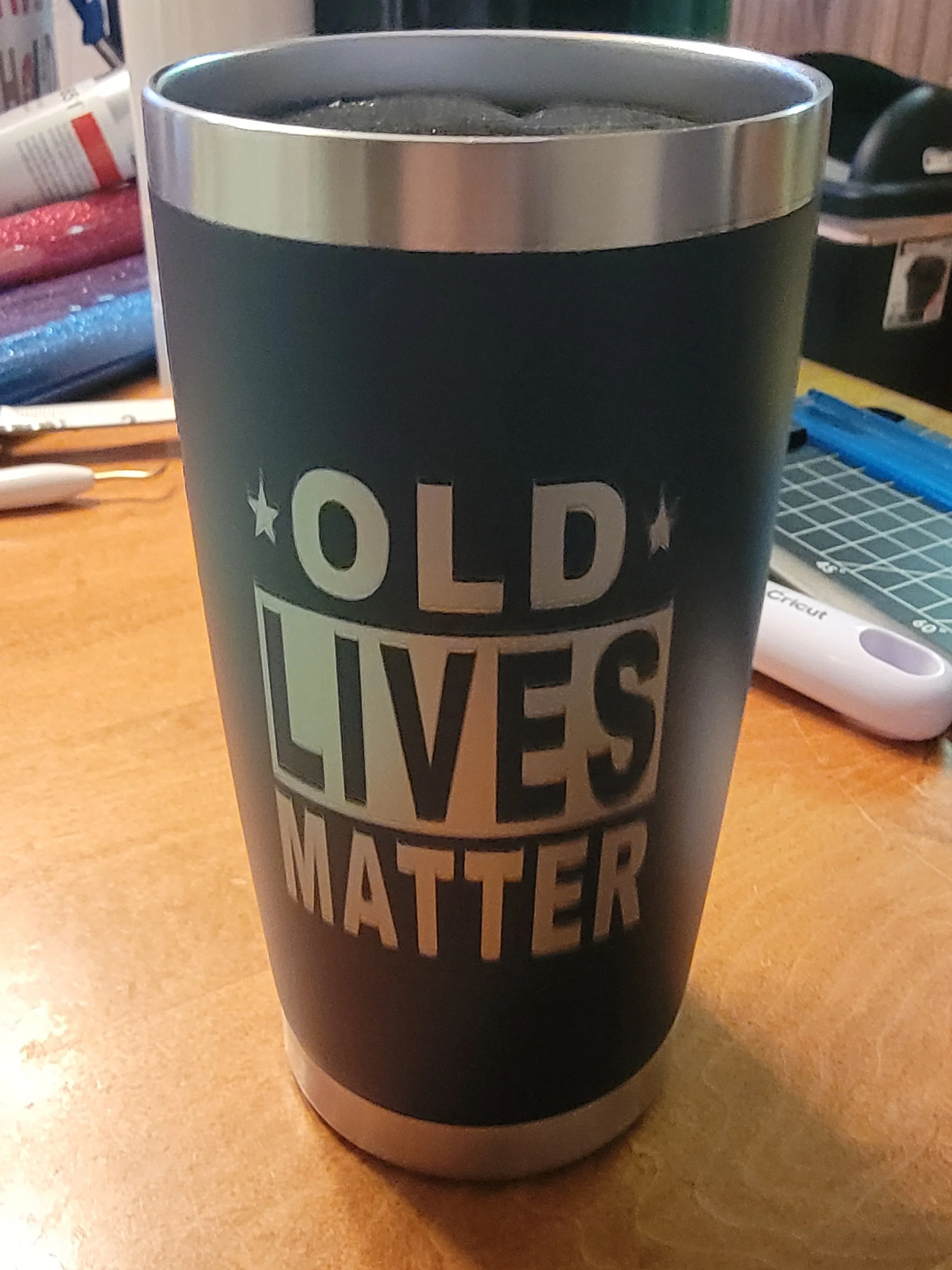 A black tumbler with a silver rim, displaying the message 'OLD LIVES MATTER' in bold, capital letters.