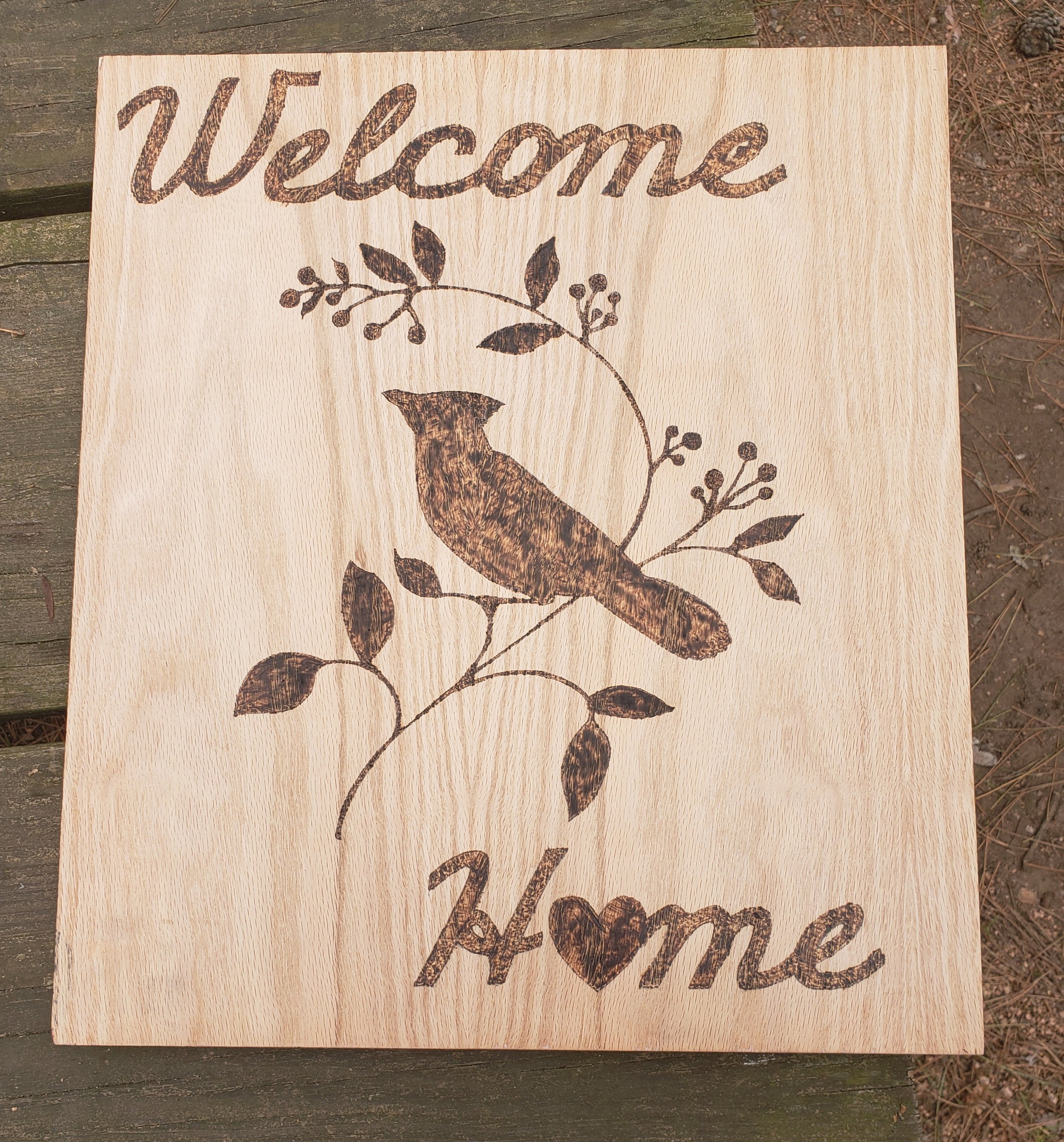 Wooden sign with a bird and botanical design, and the words "Welcome Home" engraved.