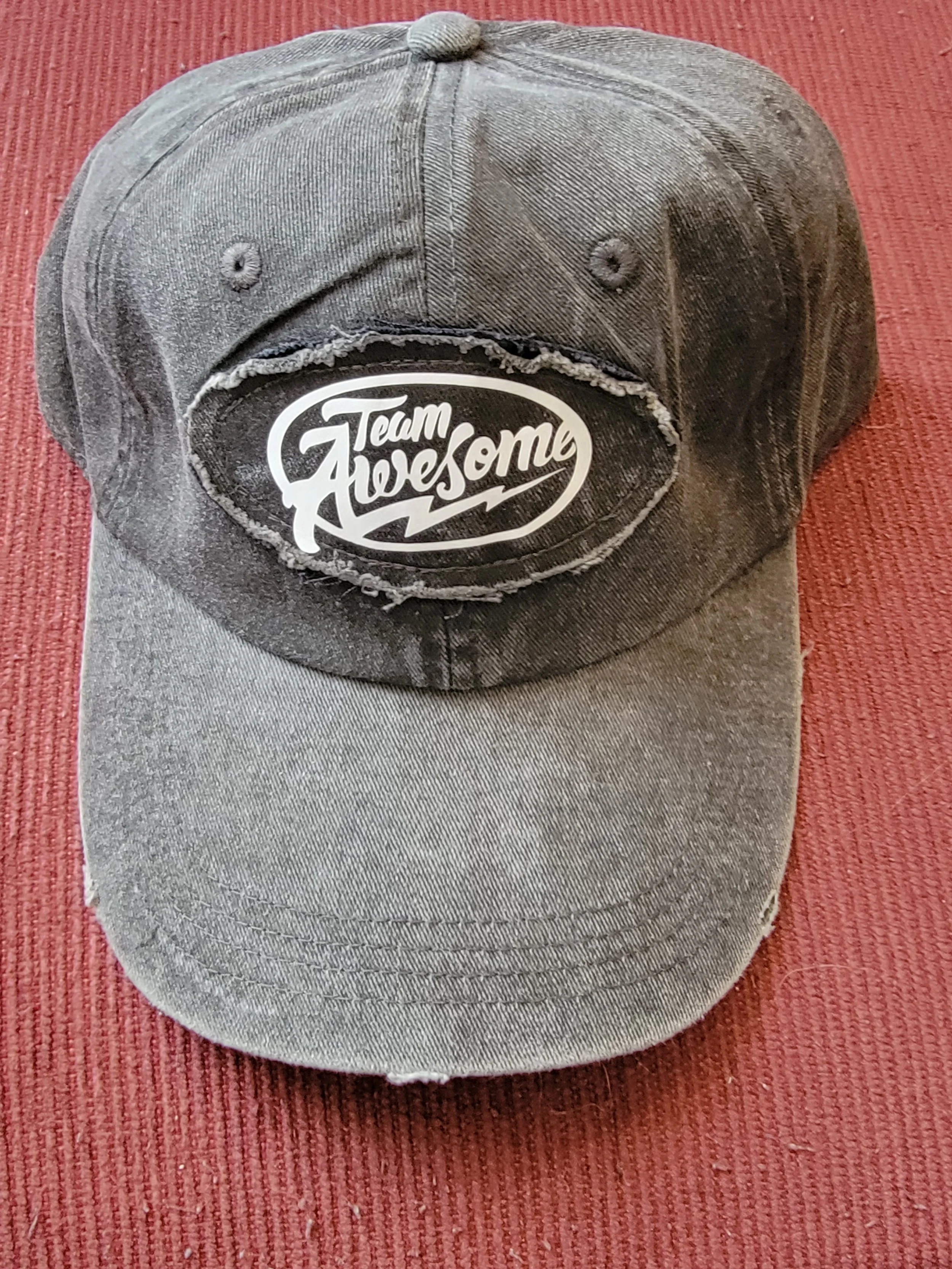 A distressed baseball cap with a black patch on the front that reads 'Team Awesome' in white lettering.