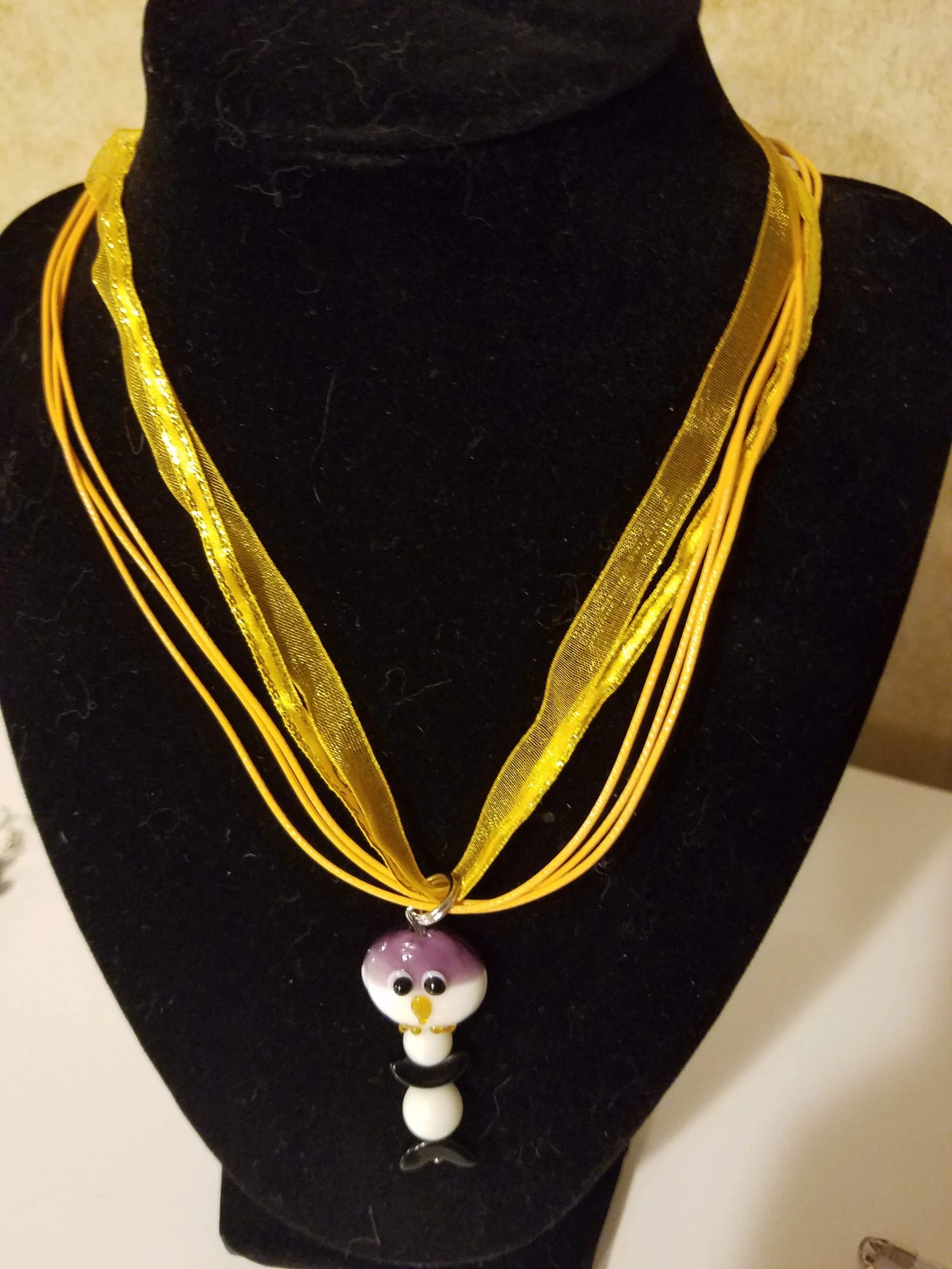 Yellow multi-strand necklace with a penguin-shaped pendant on a black display bust.