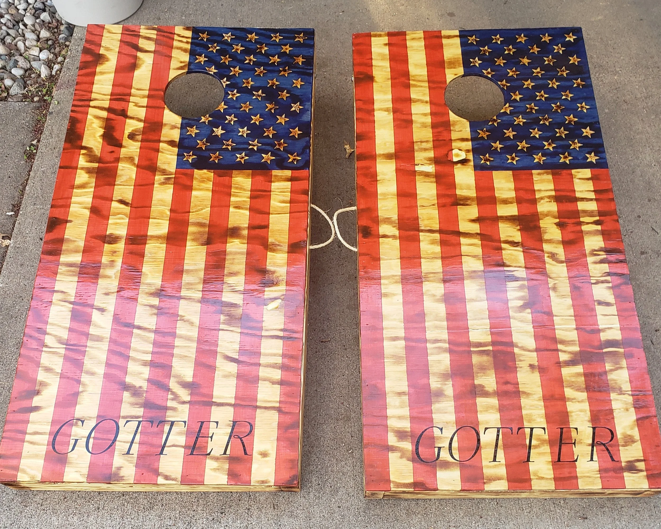 Two cornhole boards painted with American flag design and the word "GOTTER" written on each.