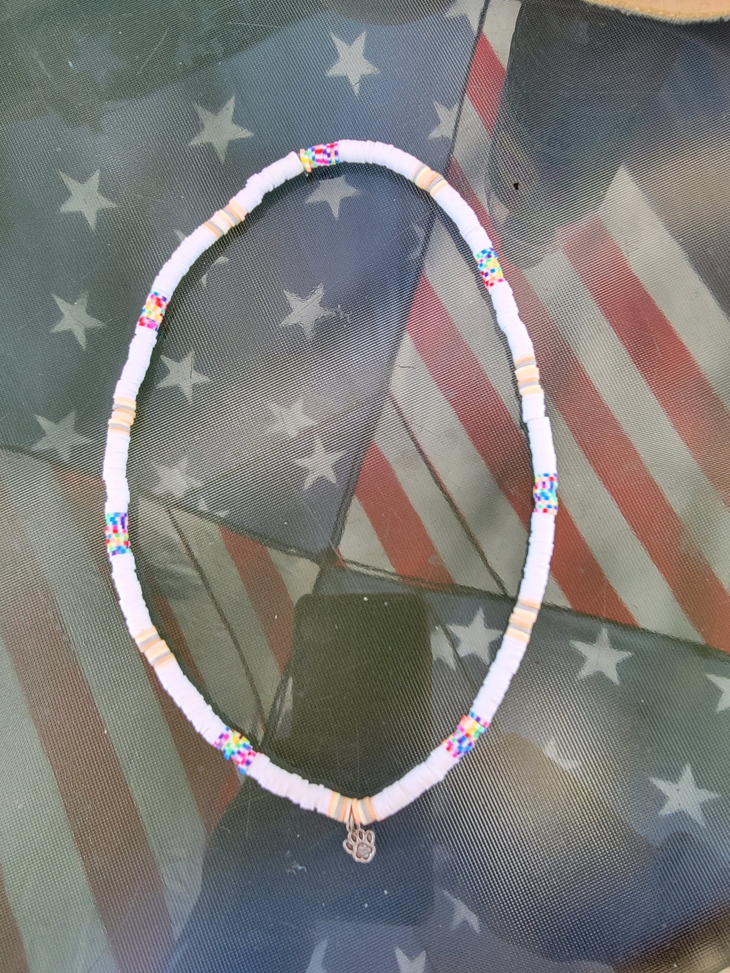 Beaded necklace with a paw print charm resting on a glass surface with American flag pattern.
