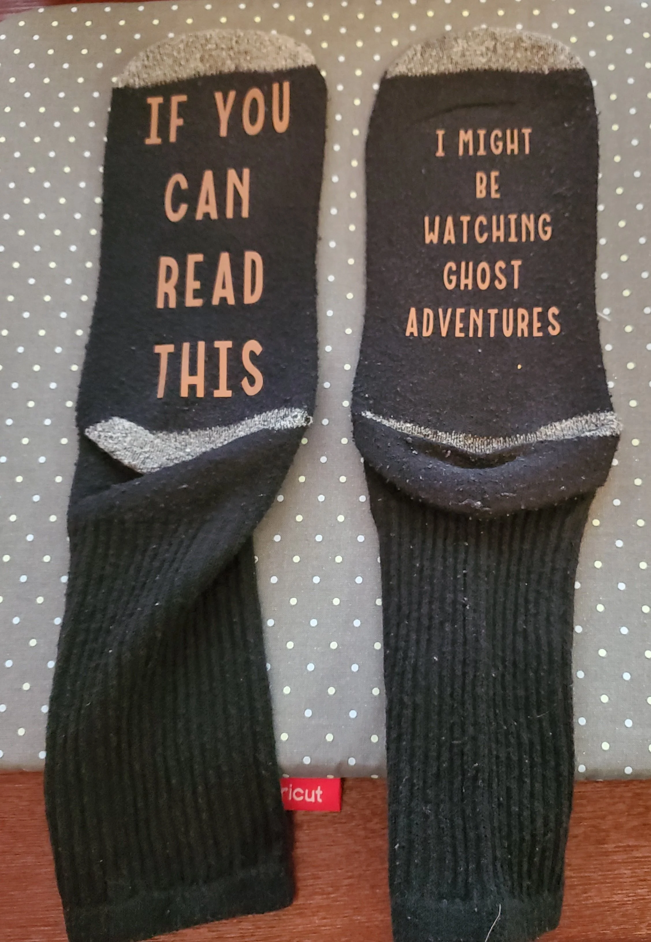 A pair of black socks with pink text, one sock says, "IF YOU CAN READ THIS," and the other says, "I MIGHT BE WATCHING GHOST ADVENTURES."