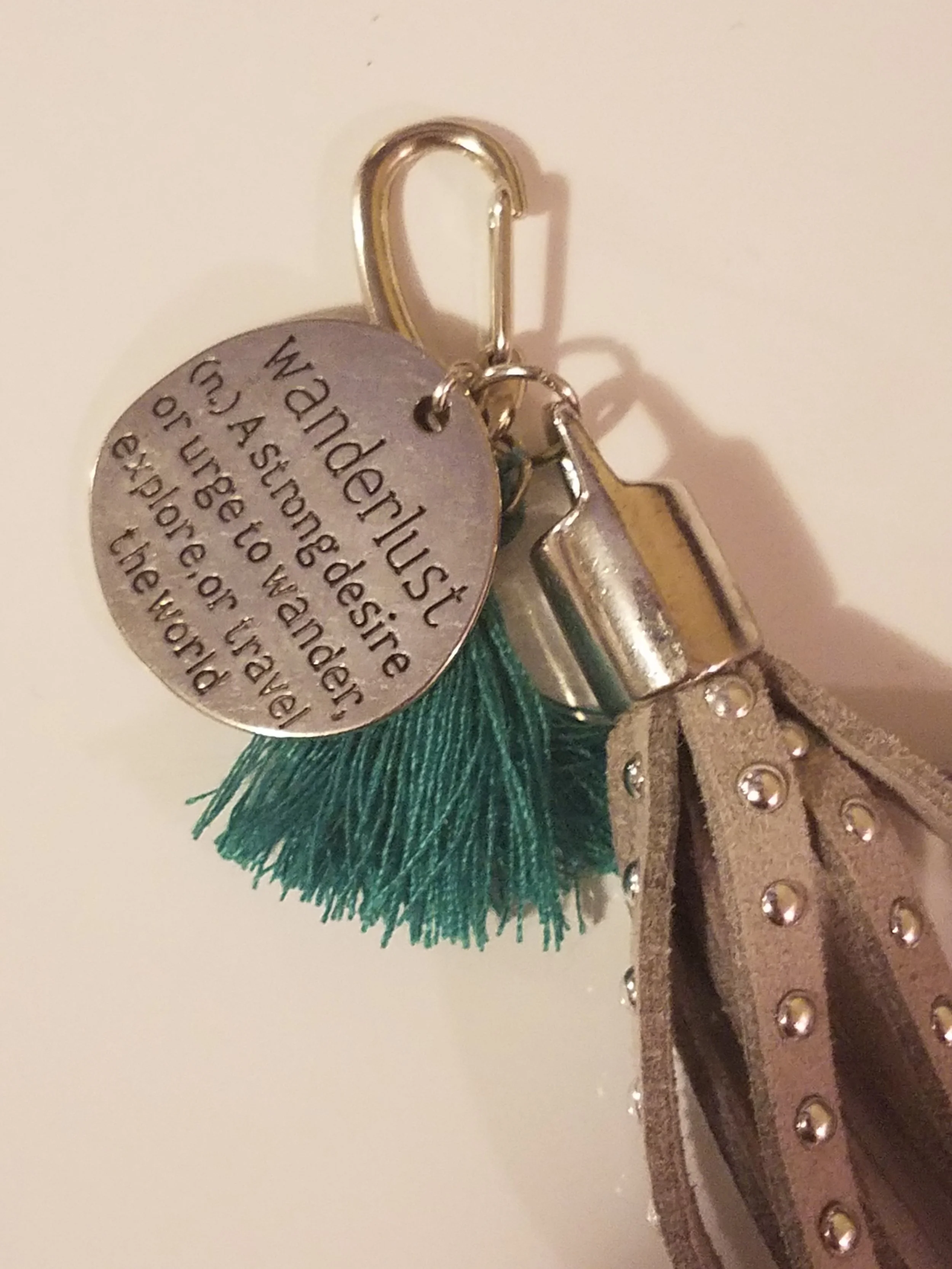 A set of keys with a grey tassel, a metallic keychain with a round engraved tag and a rectangular metal object attached.