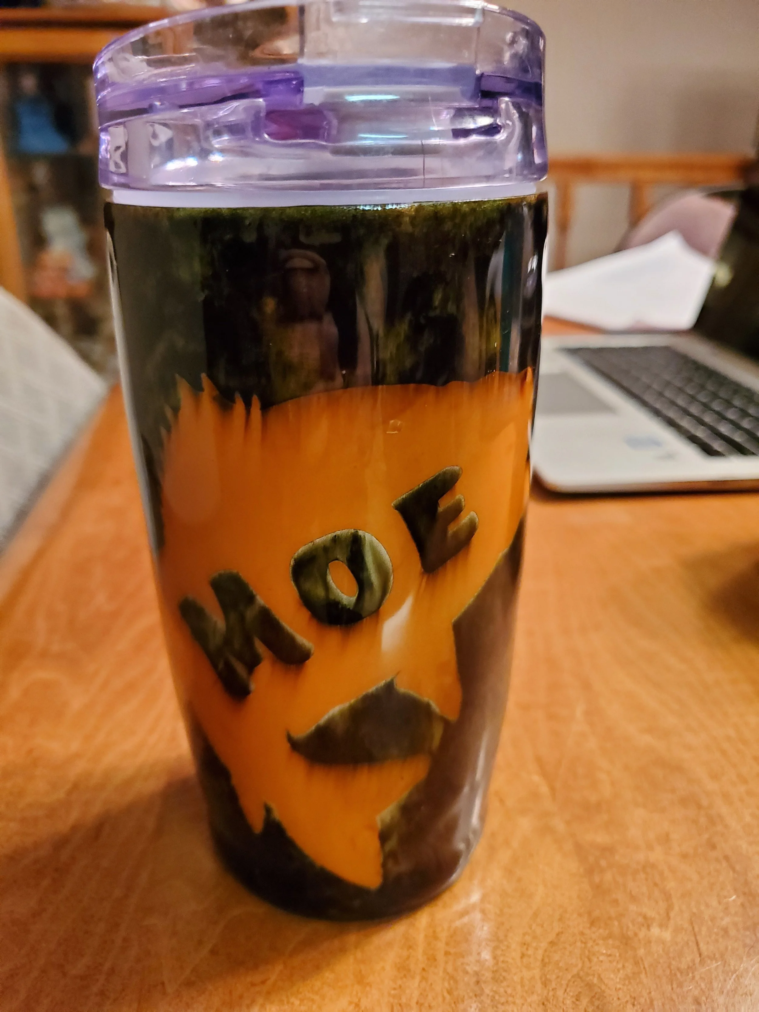 A plastic tumbler with a Halloween-themed design featuring a pumpkin face and the word 'BOO' on it, placed on a wooden table.