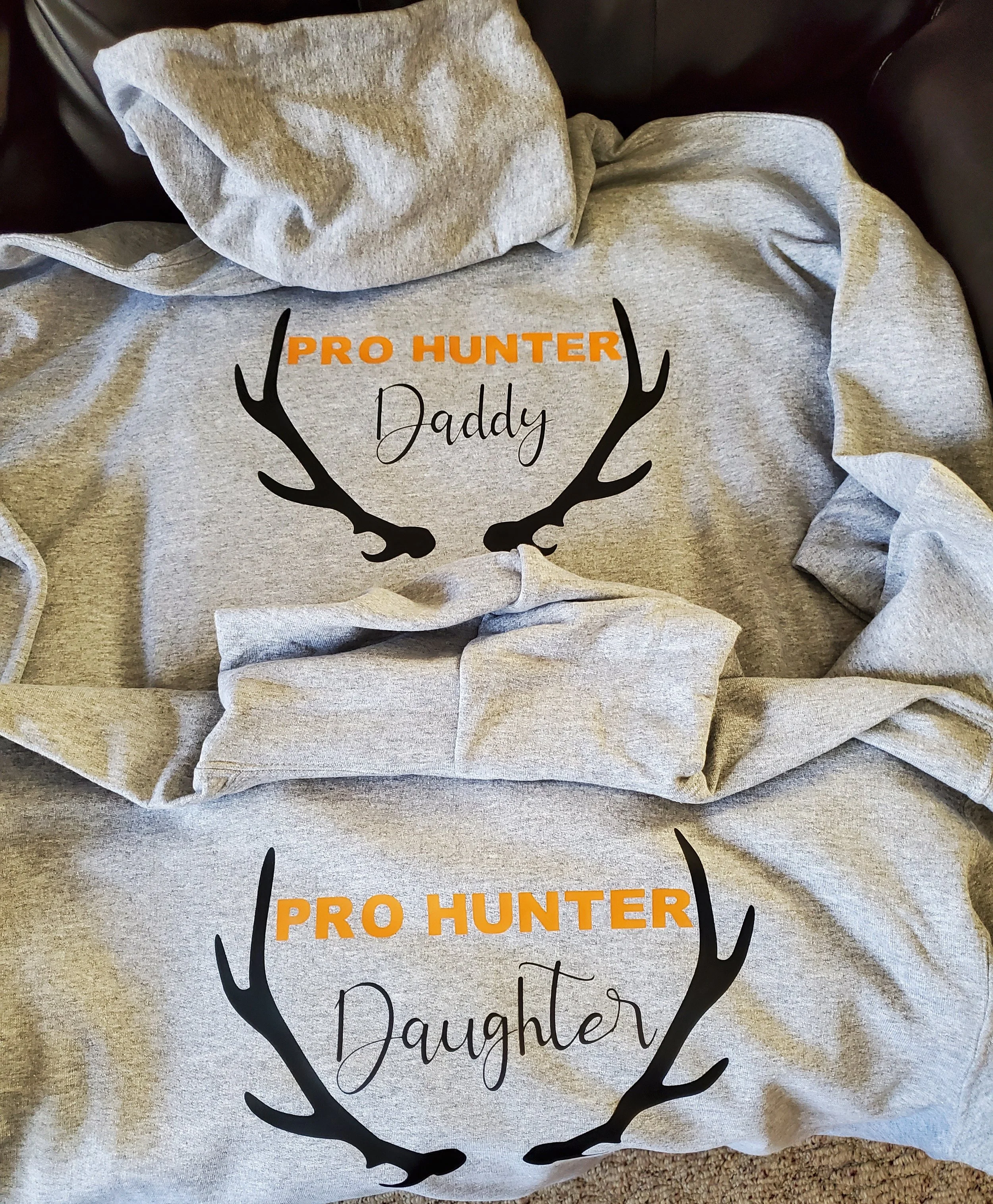 Gray hoodies with the text "Pro Hunter Daddy" and "Pro Hunter Daughter" in orange and black fonts, featuring black antler graphics.