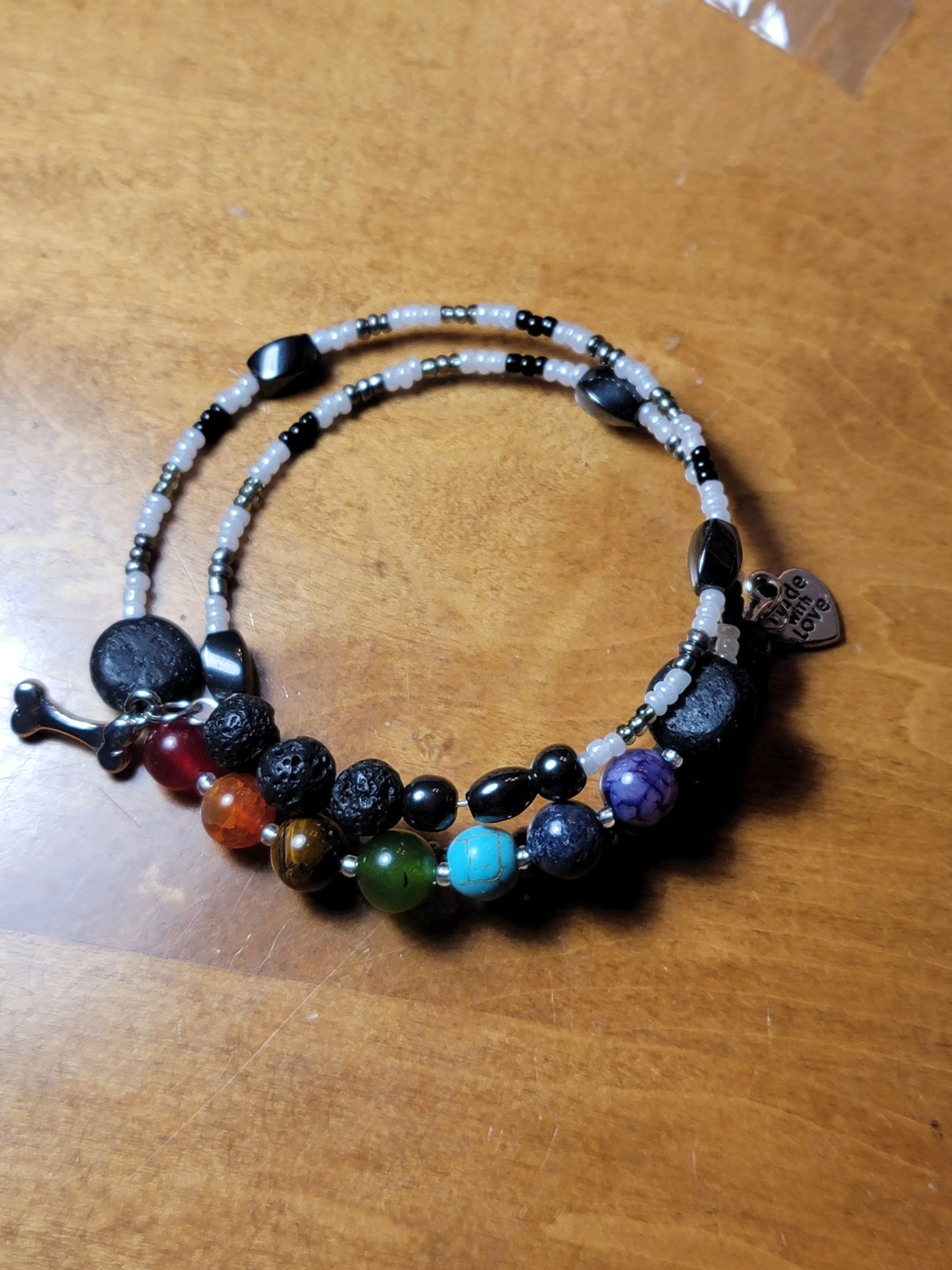 A beaded bracelet with various colorful beads, including black, turquoise, red, green, and purple, on a wooden surface, with a small heart-shaped tag that says 'made with love'.