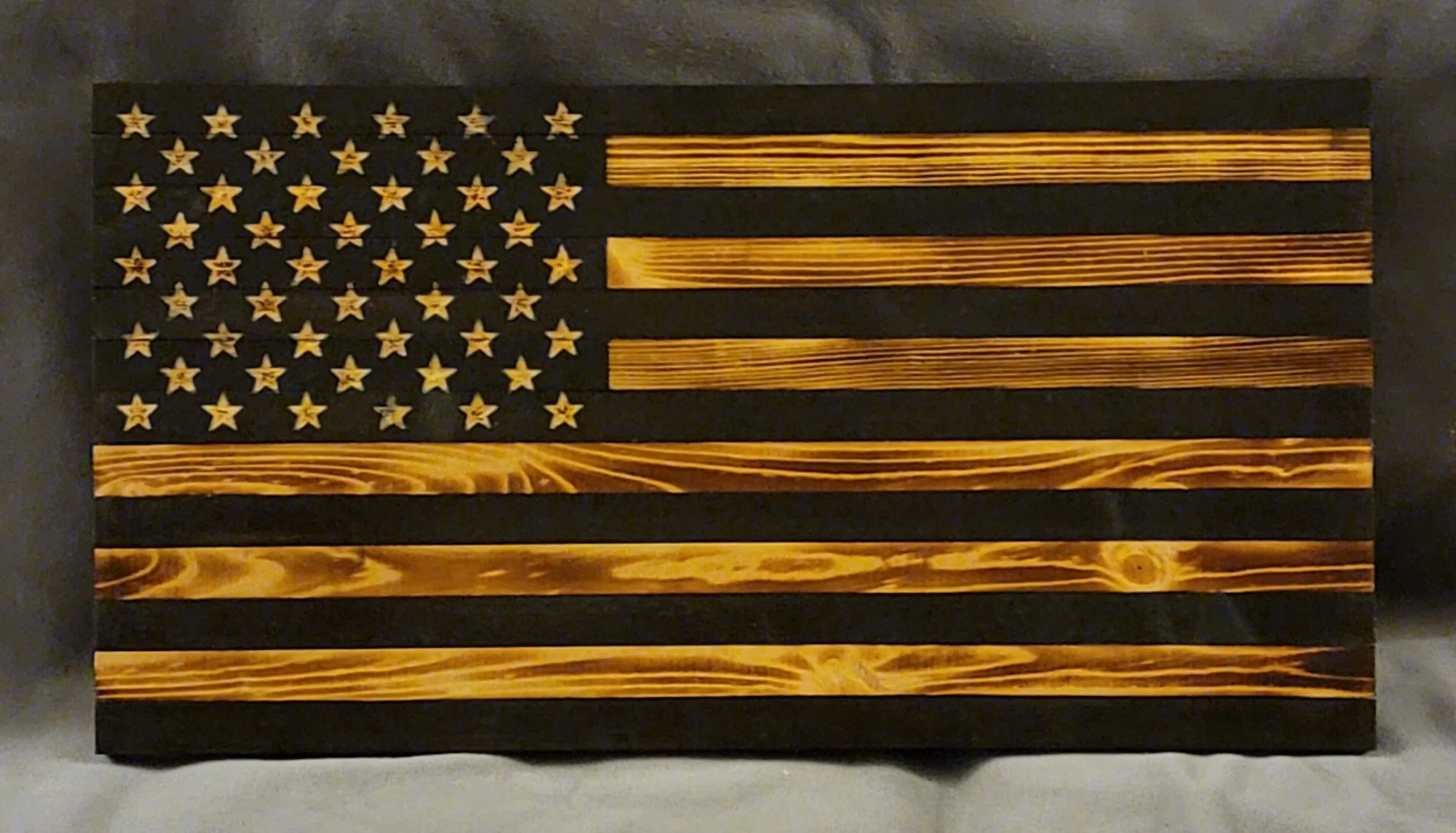 Wooden American flag with natural wood grain stars and stripes on a black background.