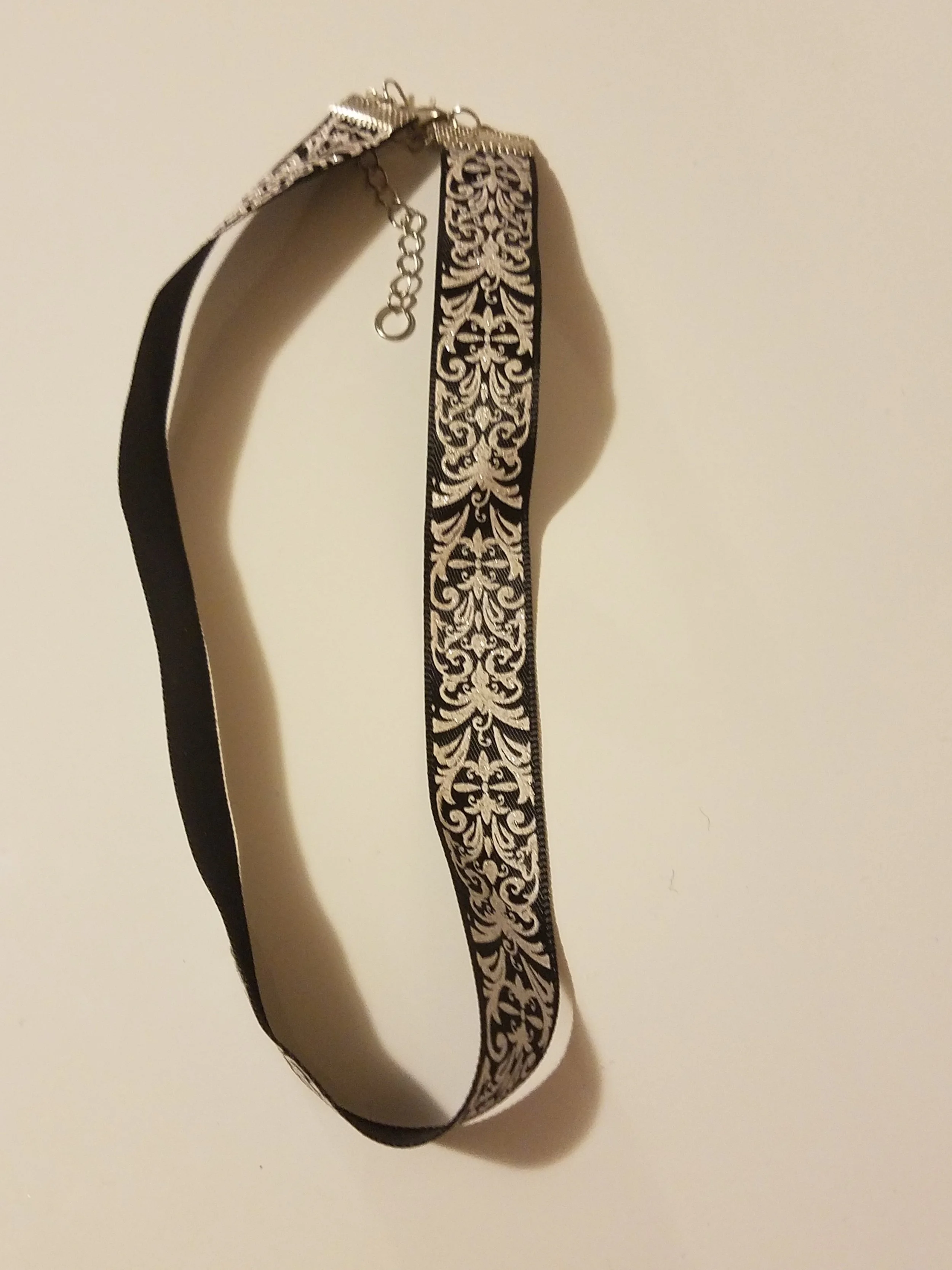 A black and white patterned choker with a silver clasp hanging against a plain white wall.