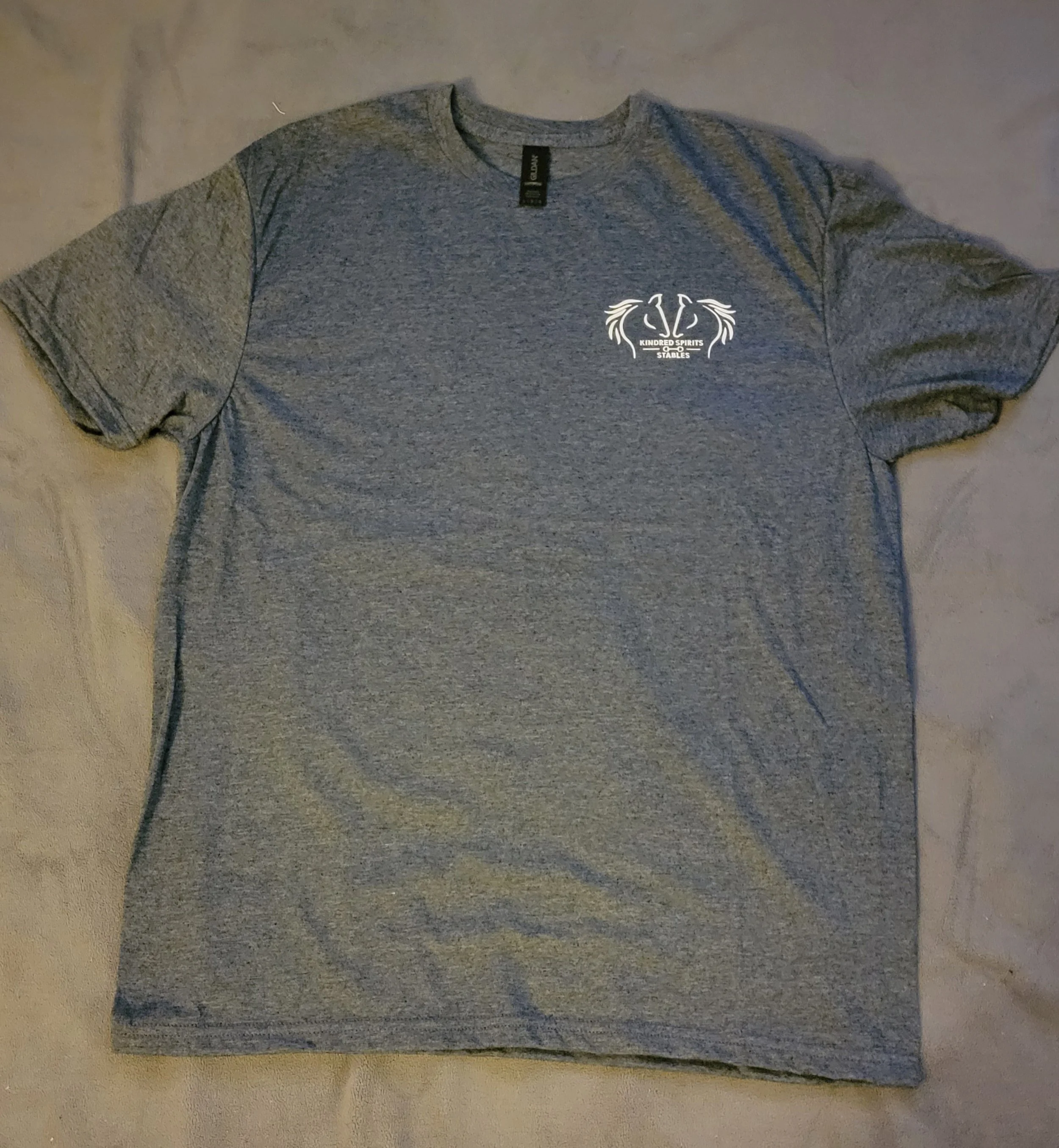 Gray T-shirt with a logo on the left chest area featuring horse heads, wings, and text that reads 'Kindred Spirits Stables'.