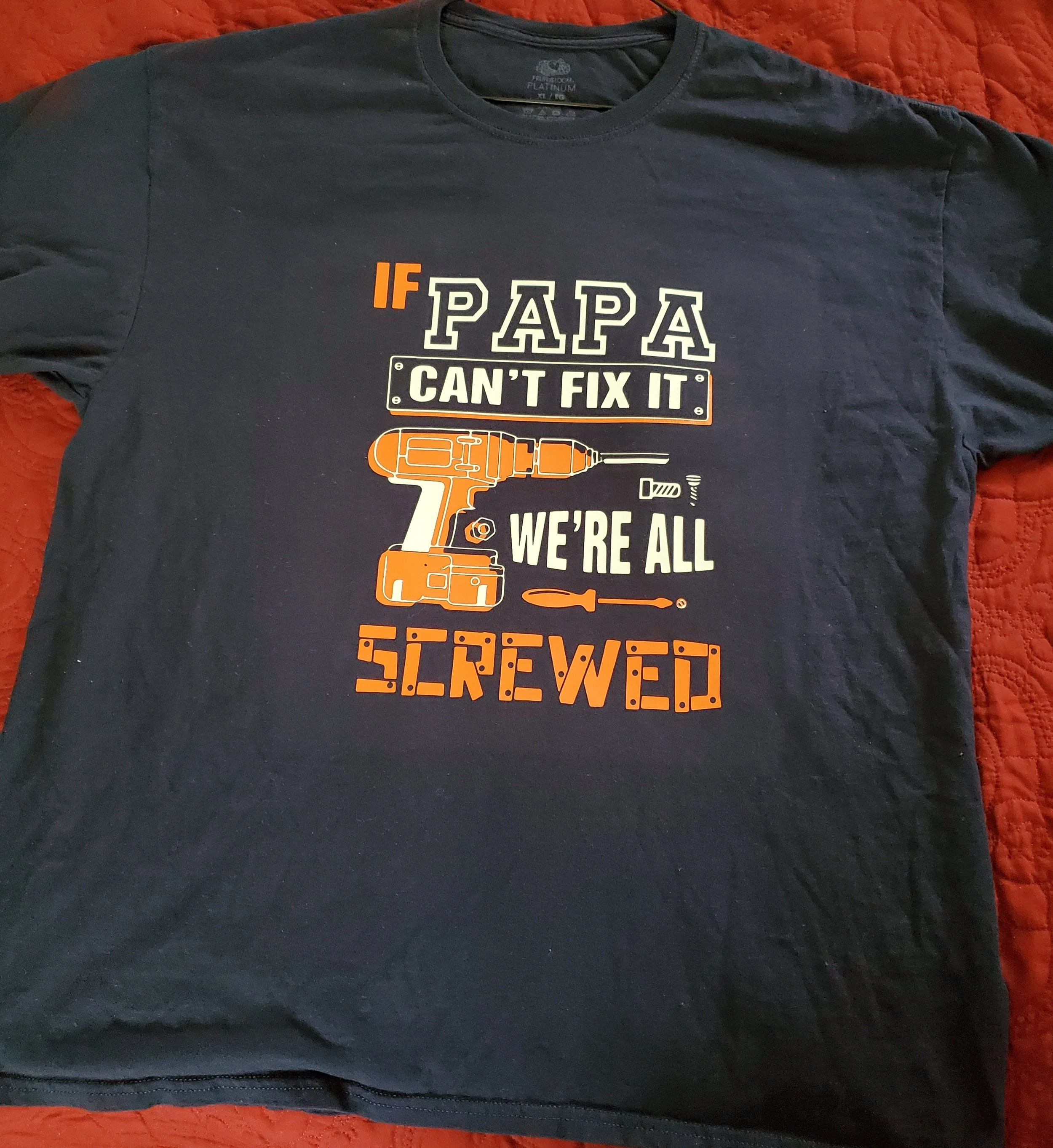A T-shirt with a humorous construction-themed message that reads, "If PAPA CAN'T FIX IT WE'RE ALL SCREWED," featuring an illustration of a cordless drill and screwdriver.
