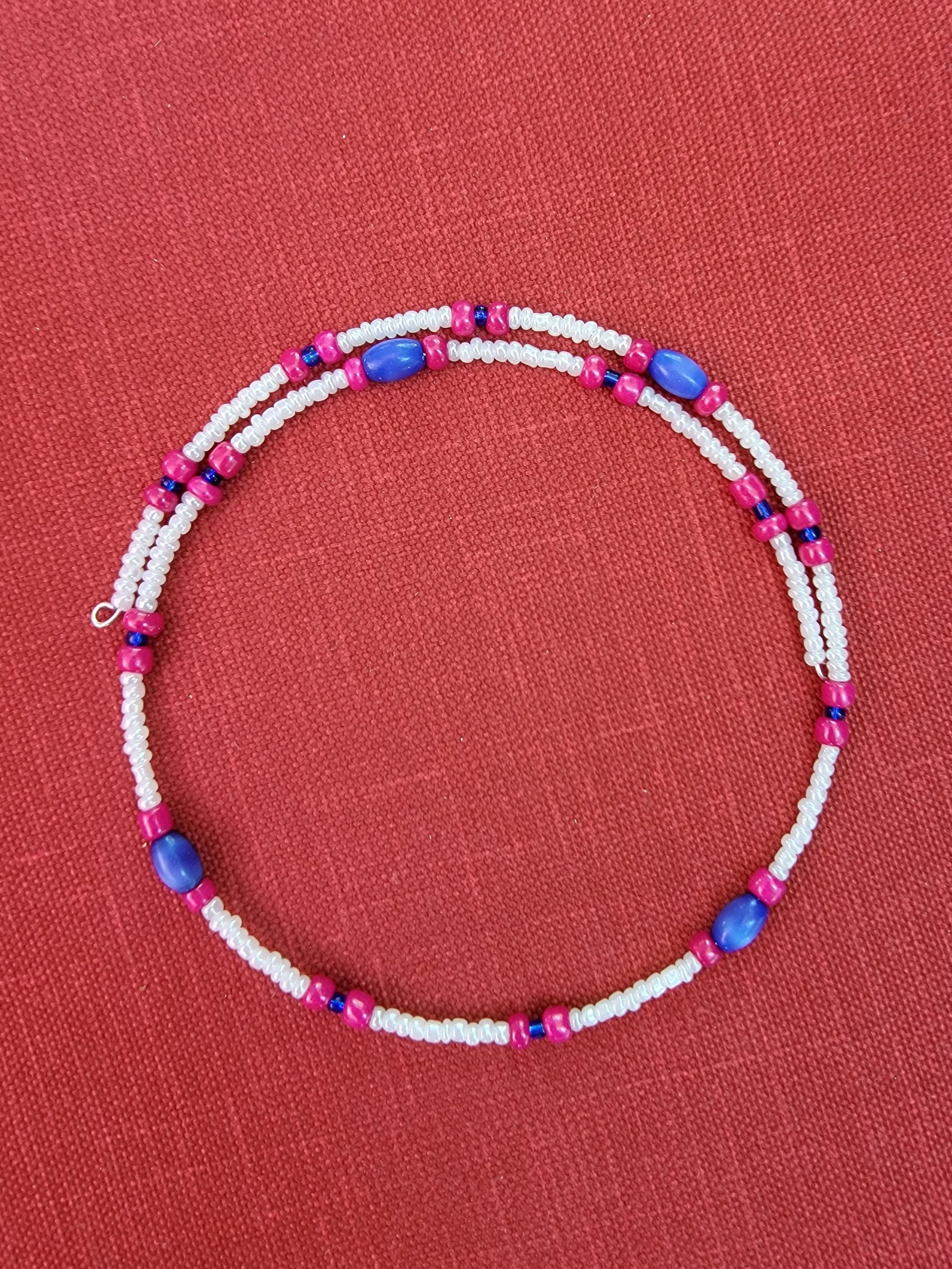 Colorful beaded necklace with white, pink, purple, and blue beads resting on a red textured background.