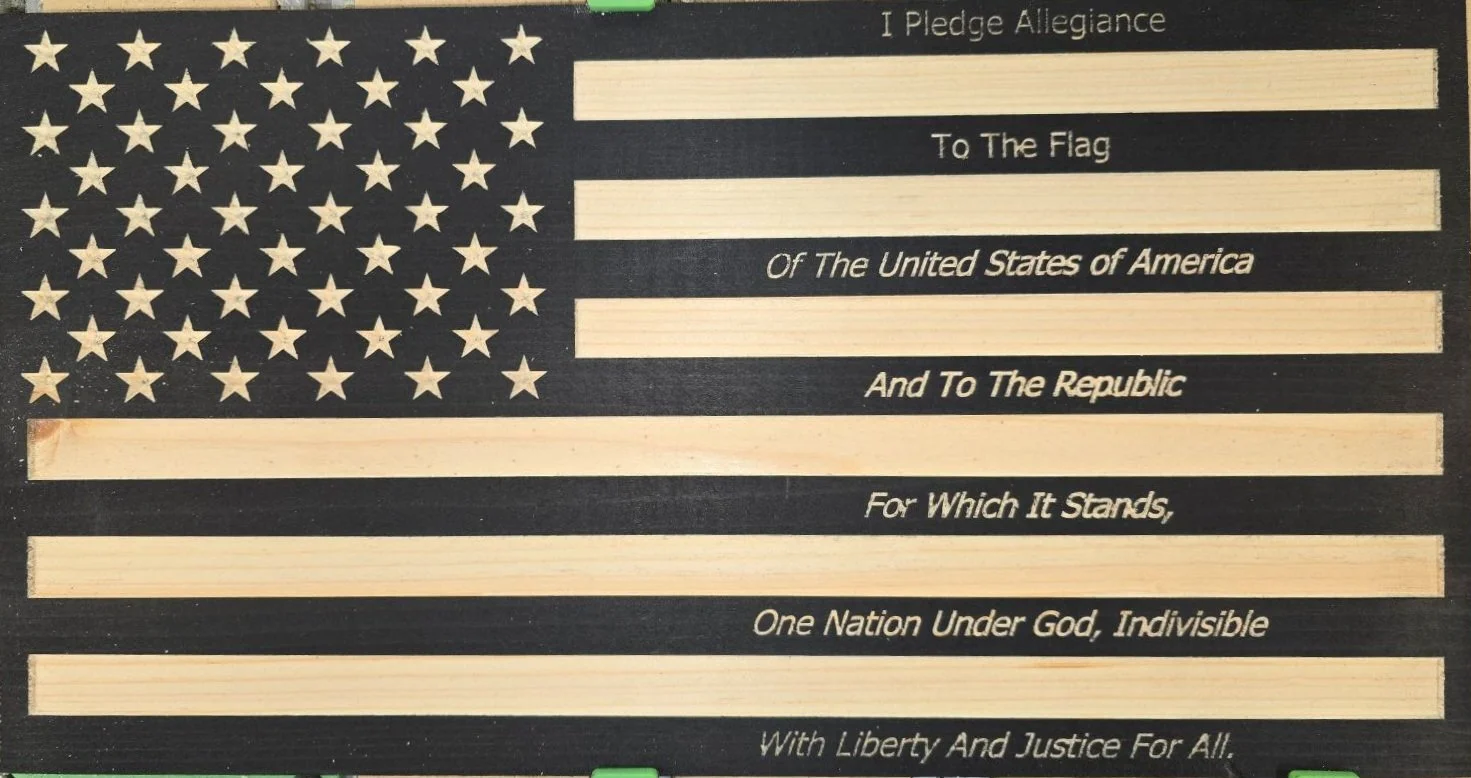 An American flag with the Pledge of Allegiance written across it, including the words 'I Pledge Allegiance To The Flag Of The United States of America And To The Republic For Which It Stands, One Nation Under God, Indivisible With Liberty And Justice