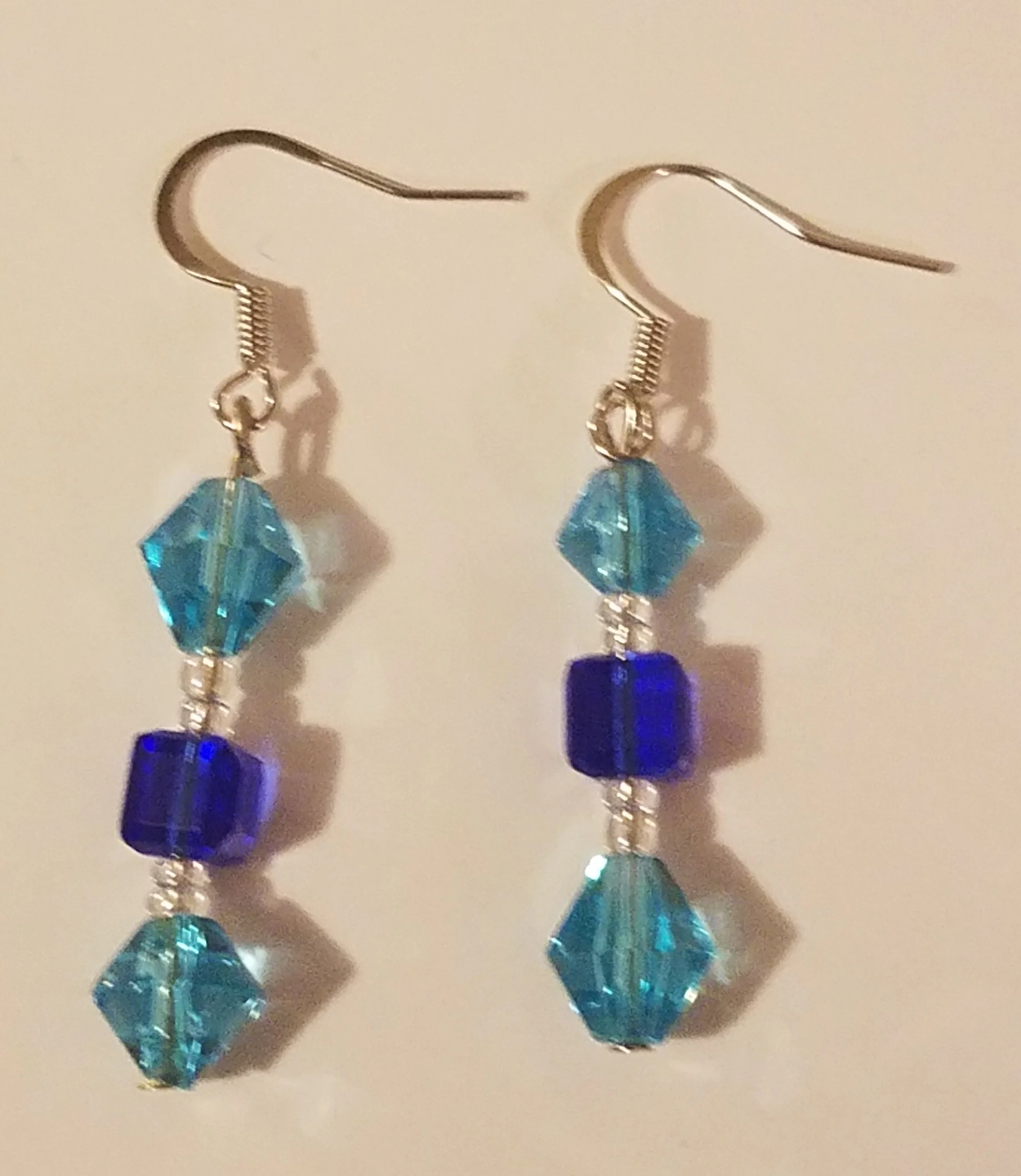 A pair of dangle earrings with blue and aqua faceted beads hanging from silver hooks.
