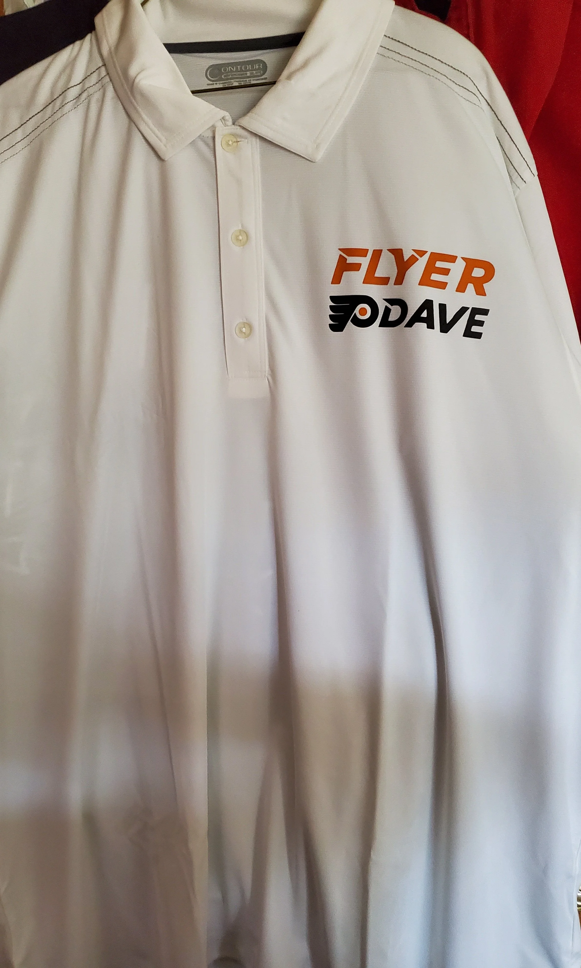 A white polo shirt with a collar and button placket, featuring logos for 'Flyer' in orange and 'DAVE' in black with a stylized winged 'D', hanging on a rack.