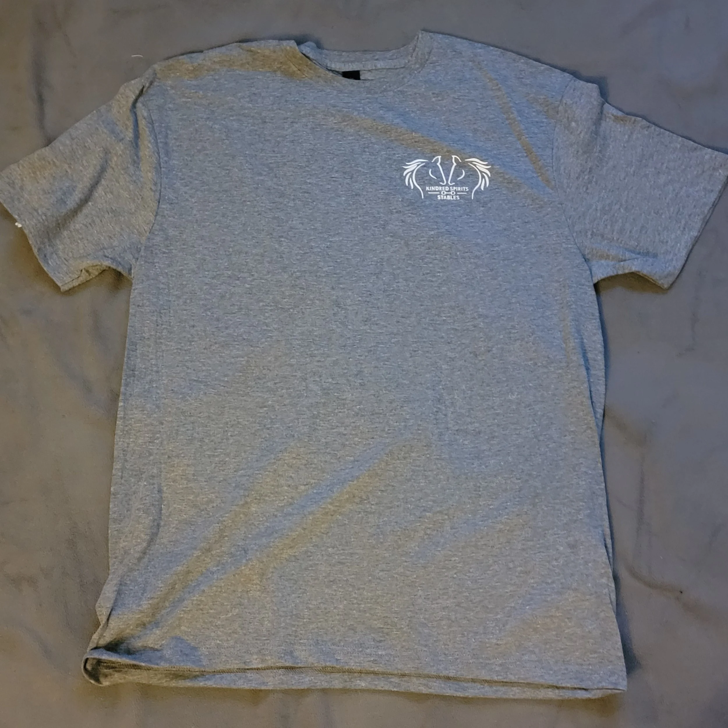 Gray T-shirt with a small logo on the left chest area that reads 'Kindred Spirits' with additional text underneath and a decorative design.