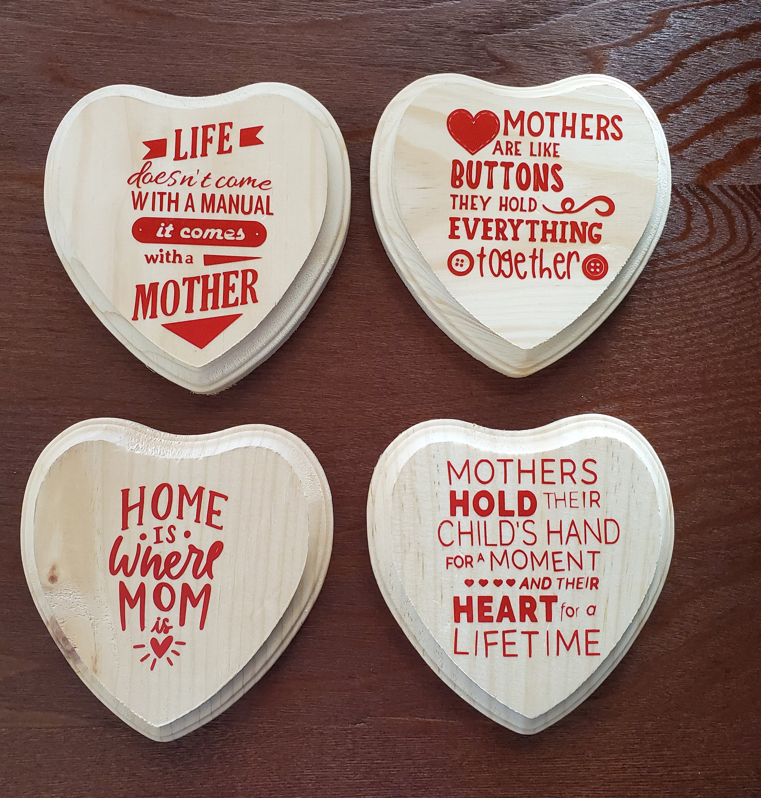 Four heart-shaped wooden plaques with red printed quotes about motherhood, placed on a wooden surface.
