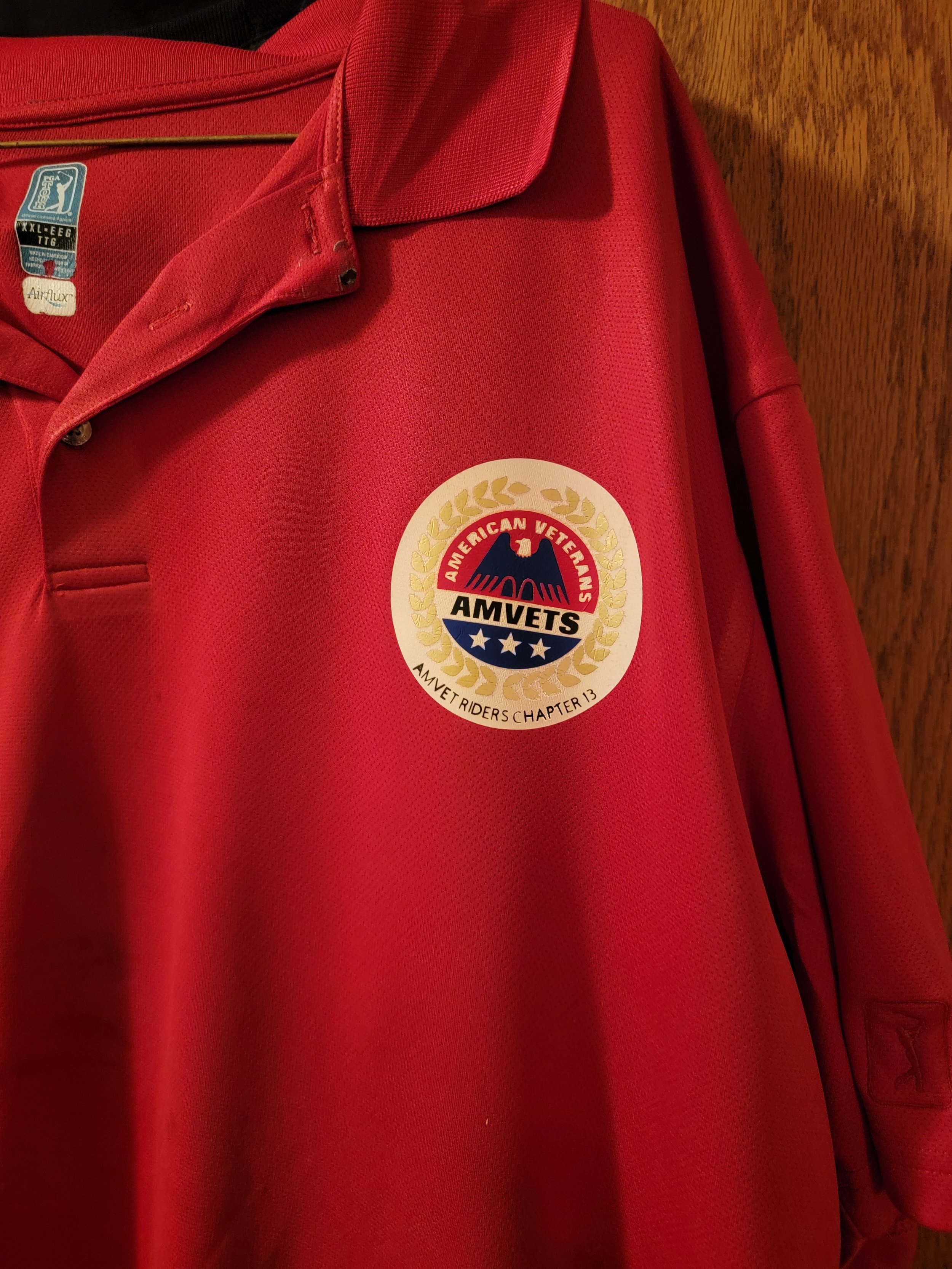 Red jacket with an embroidered patch of the American Veterans AMVETS organization on the chest, featuring a bald eagle, stars, and a laurel wreath.