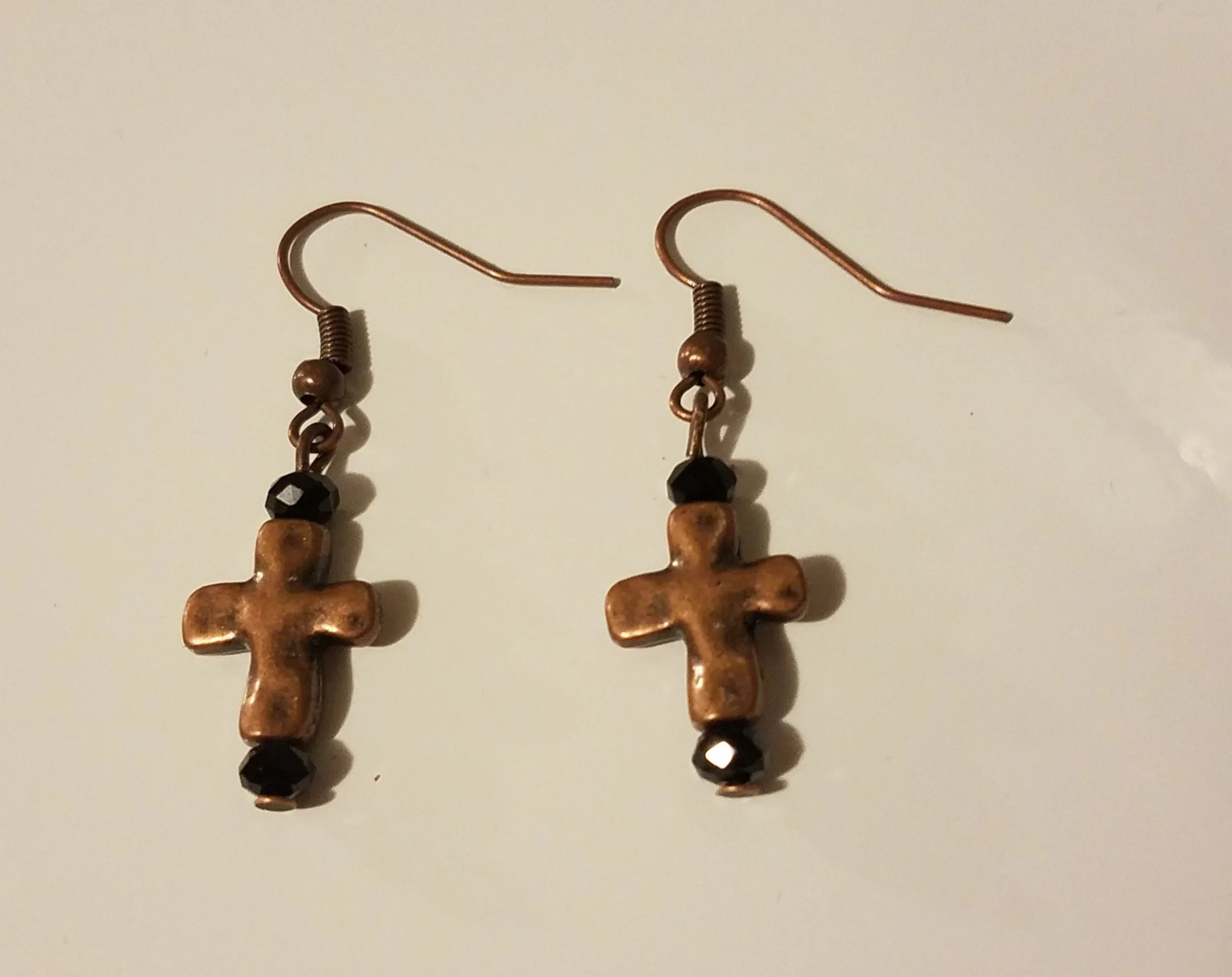 Earrings with crucifix charms and black beads hanging from copper hooks.