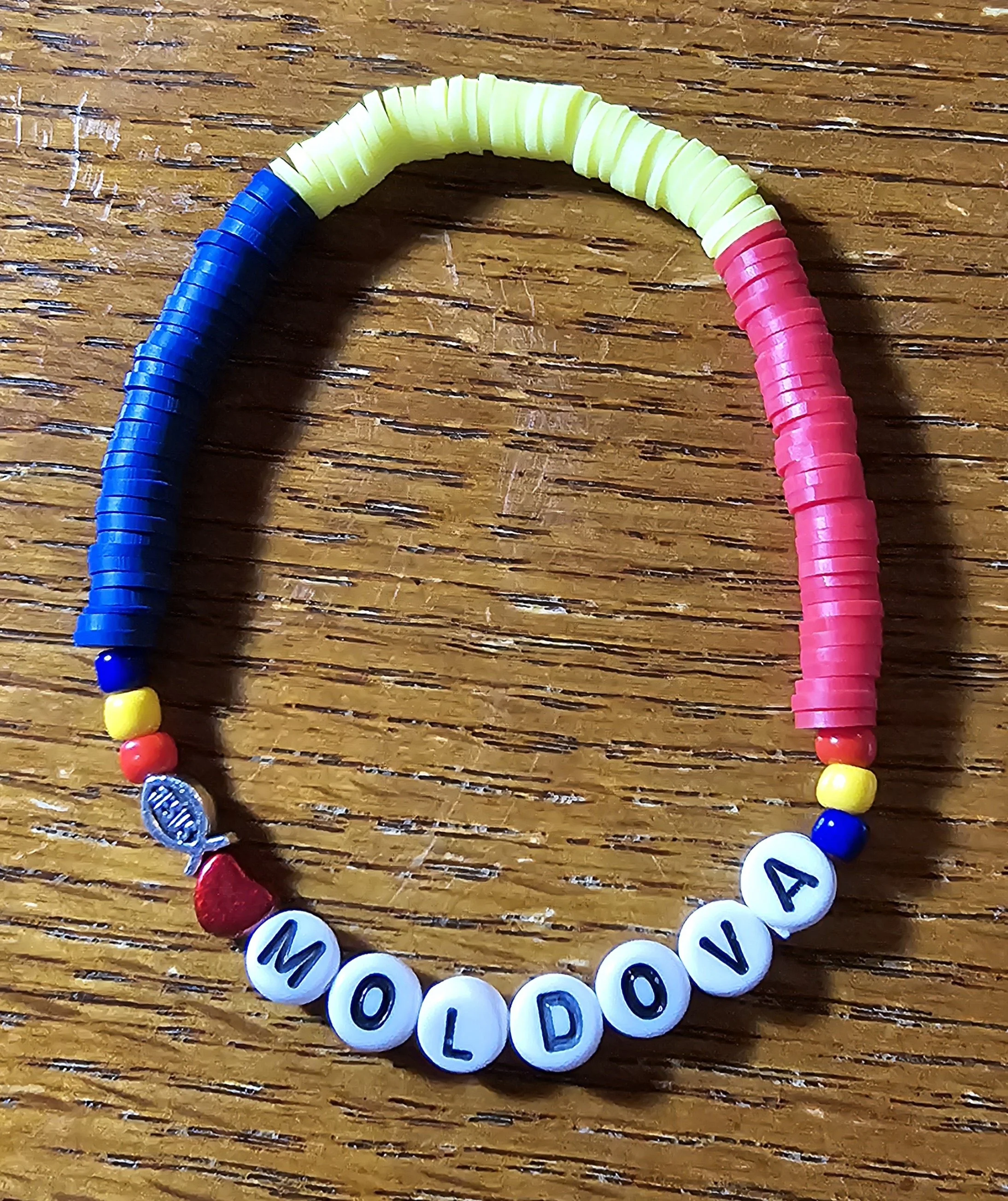 Colorful beaded bracelet spelling out 'MOLDOVA' with rainbow colors on a wooden surface.