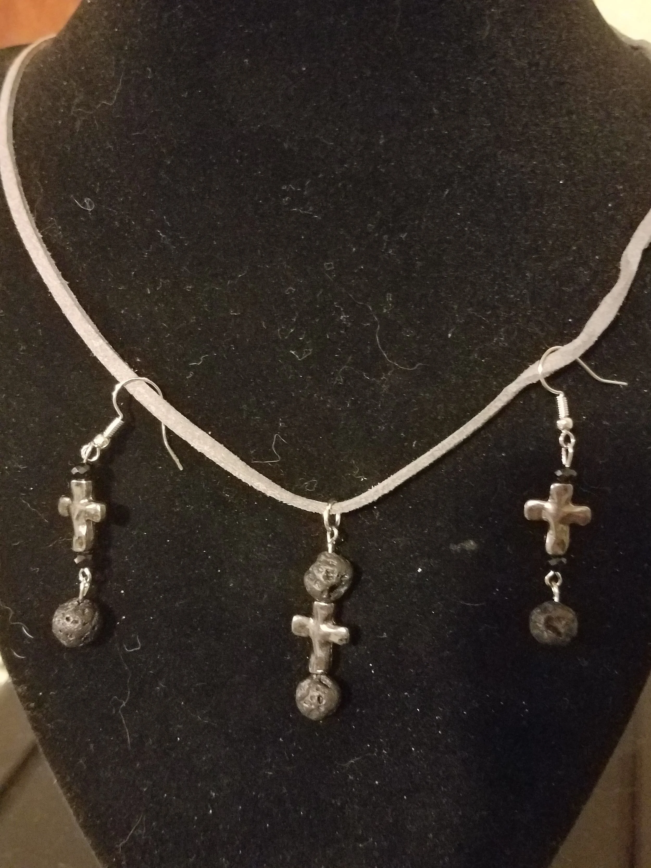 A necklace and earrings jewelry set with silver cross pendants and spherical bead charms, displayed on a black jewelry bust.