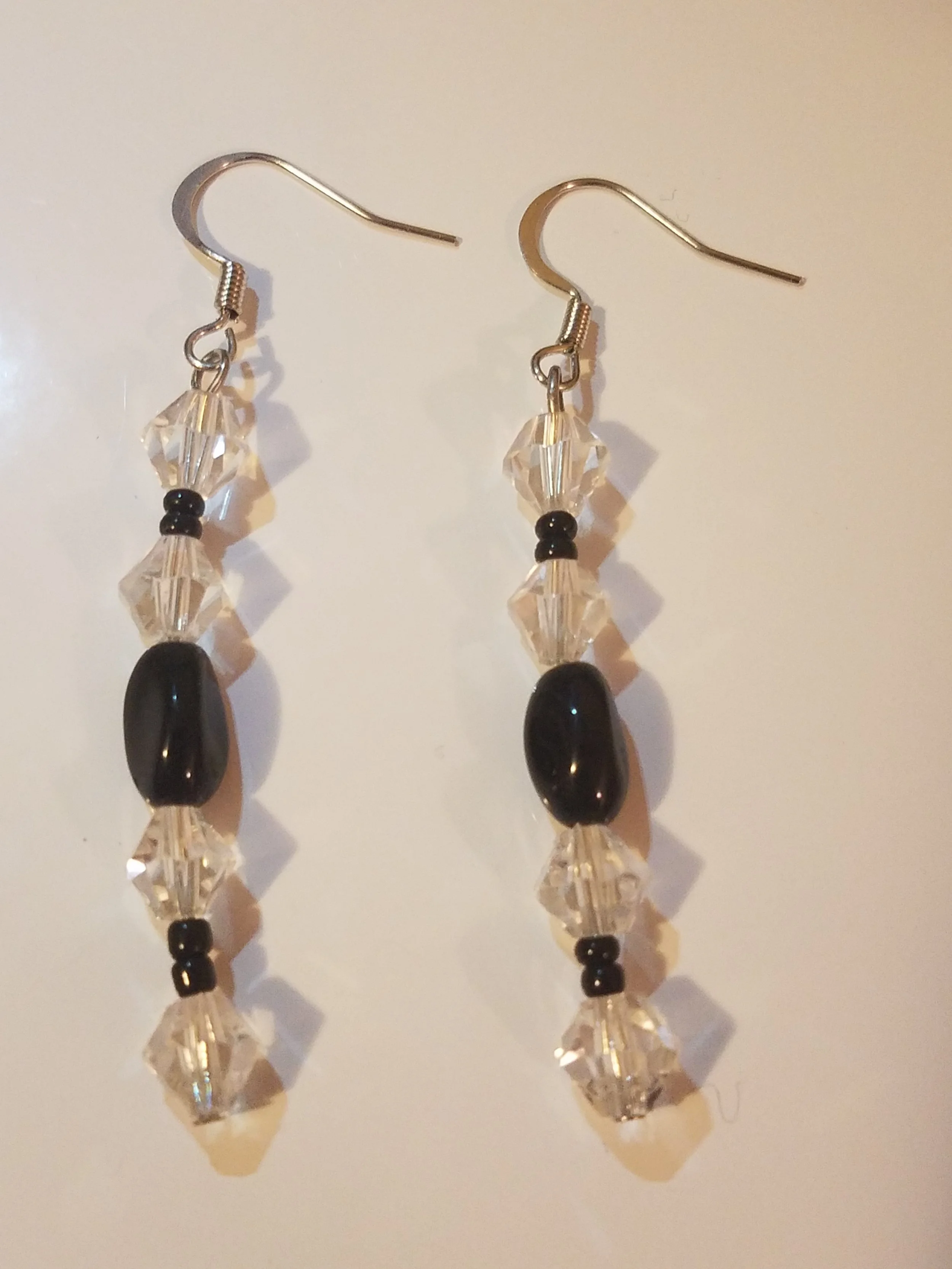 Pair of dangling earrings with black and clear beads, including one large black bead and several smaller clear beads, hanging from silver hooks.